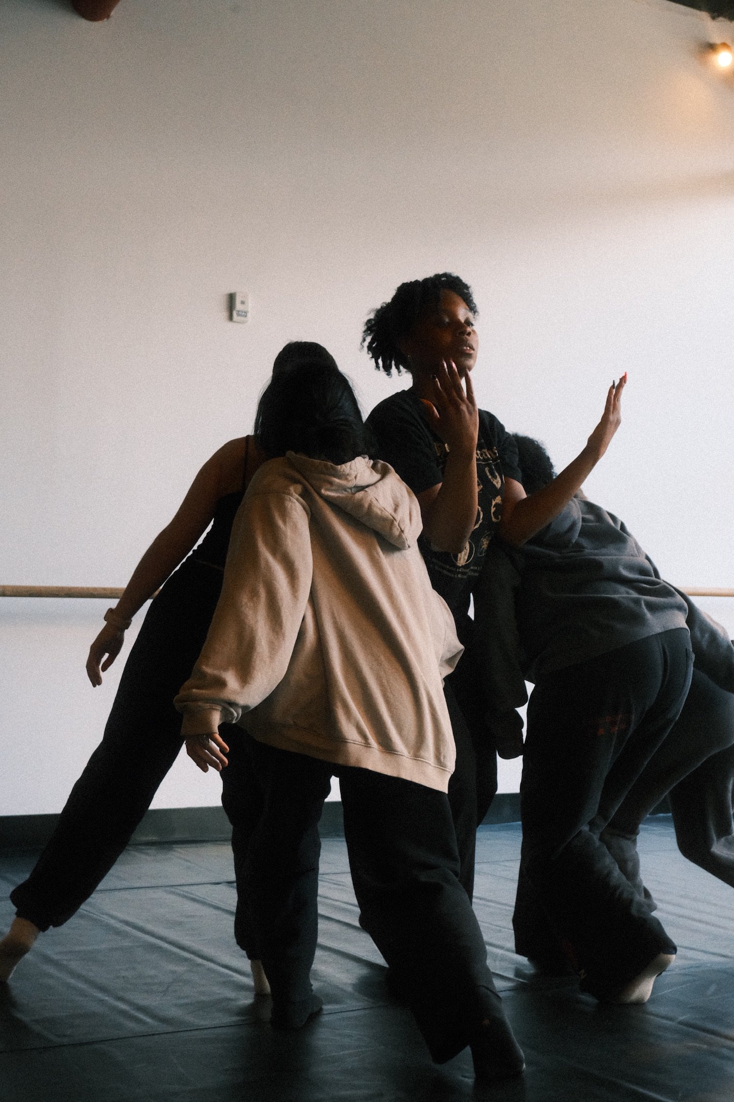 Three people practicing dance or exercise in a studio with a white brick wall and red abstract art.