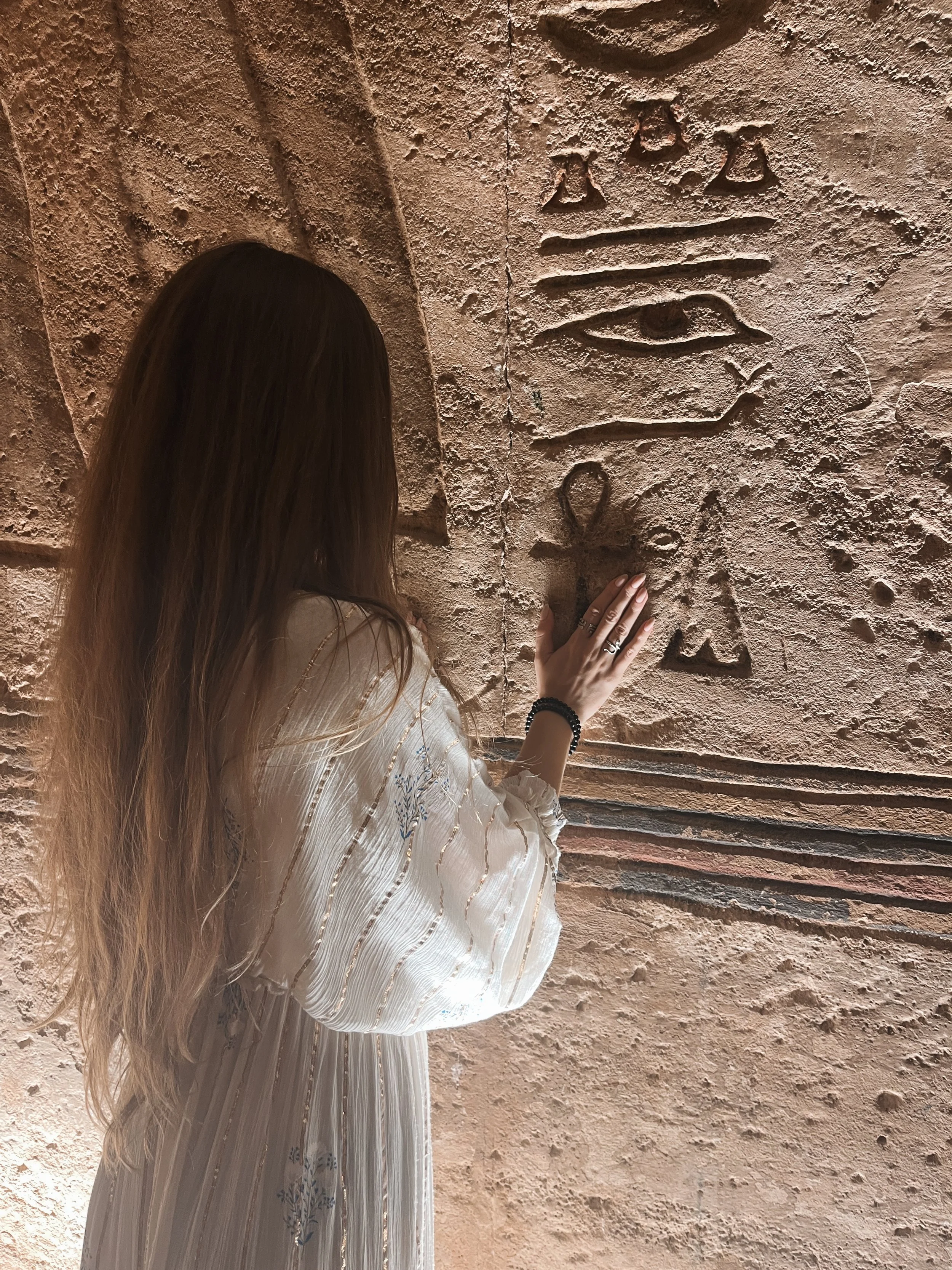 Sabina's hand touching an ankh symbol carved into an ancient Egyptian temple wall surrounded by hieroglyphs