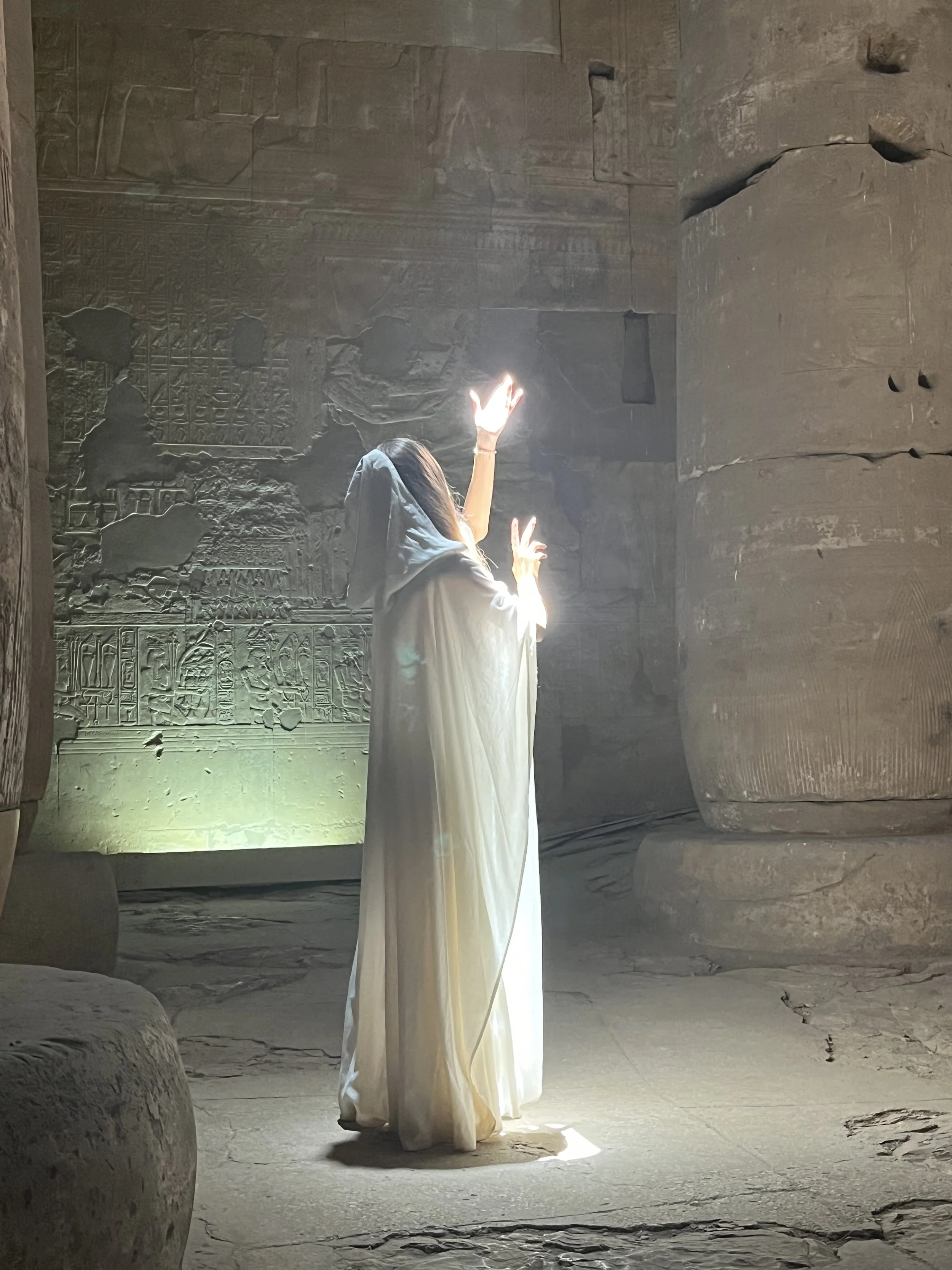 Sabina in white robe channeling Light Codes with glowing hand raised inside Abydos temple during a sacred ceremony