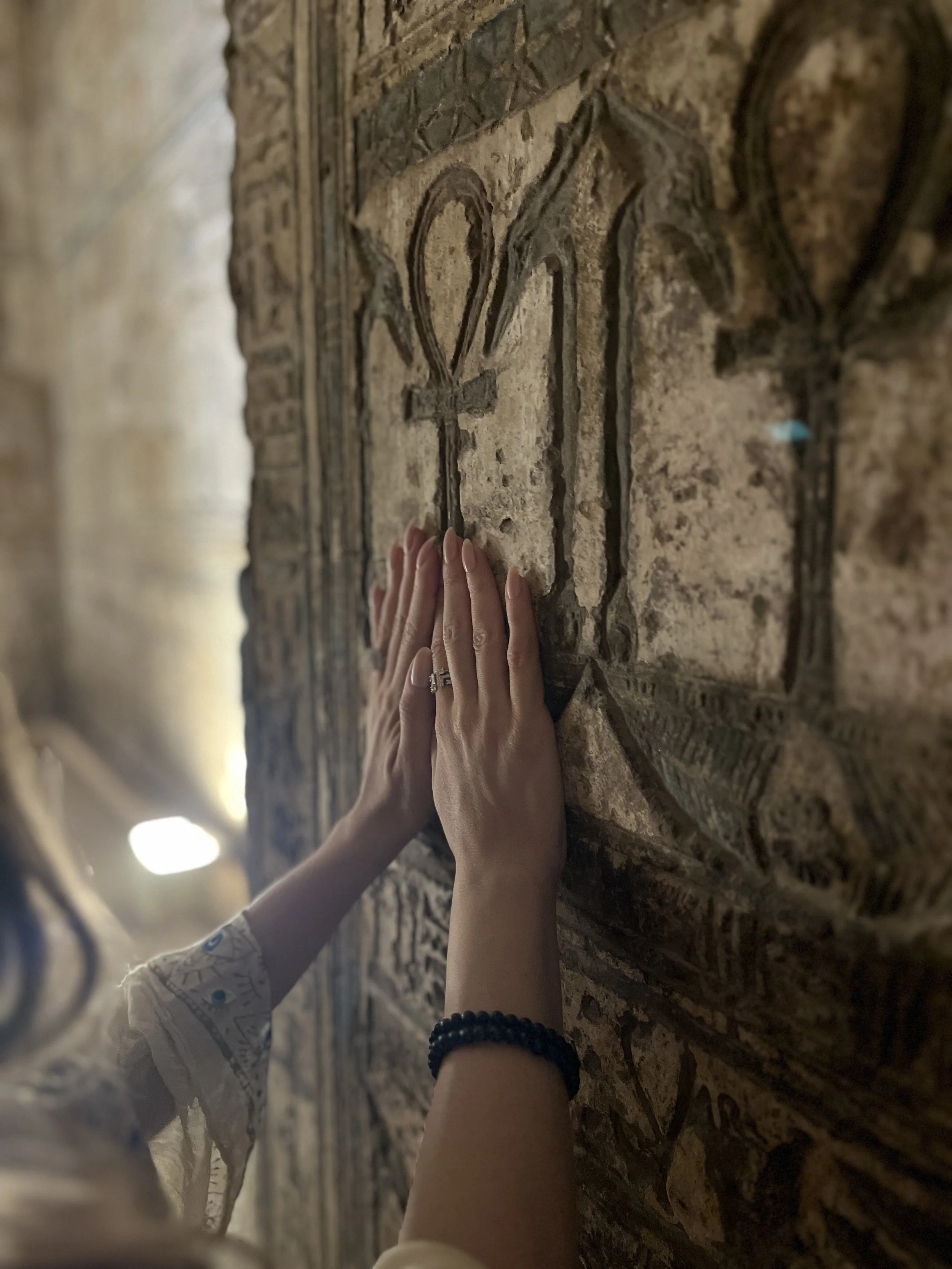 Two hands touching an ankh symbol carved into the ancient stone wall of an Egyptian temple at Abydos