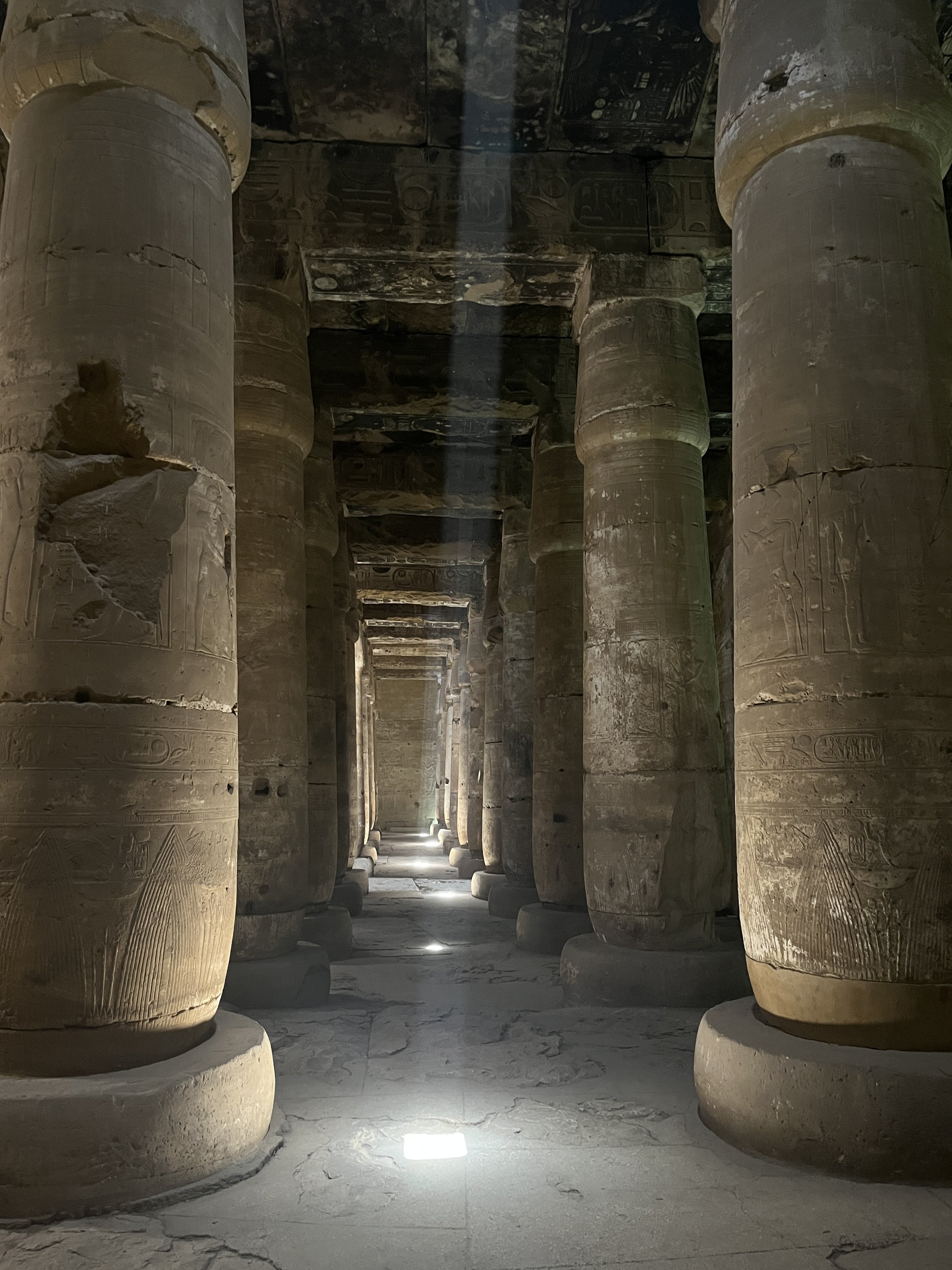 Long corridor inside the Temple of Seti I at Abydos with massive ancient columns covered in hieroglyphs and streams of light coming through the ceiling