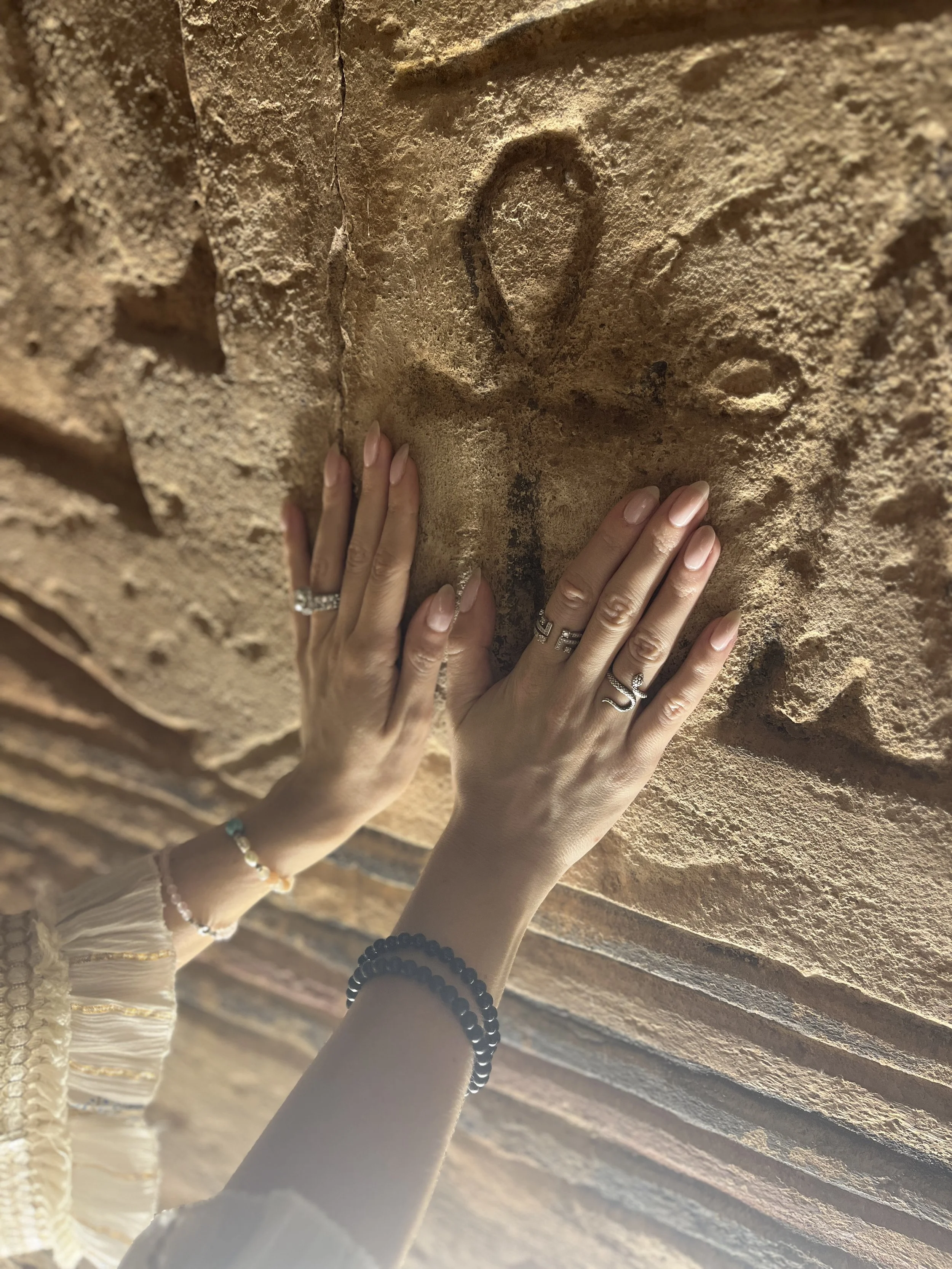 Close-up of woman's hands on ankh symbol carved on ancient Egyptian stone symbolizing energy alignment and soul remembrance.