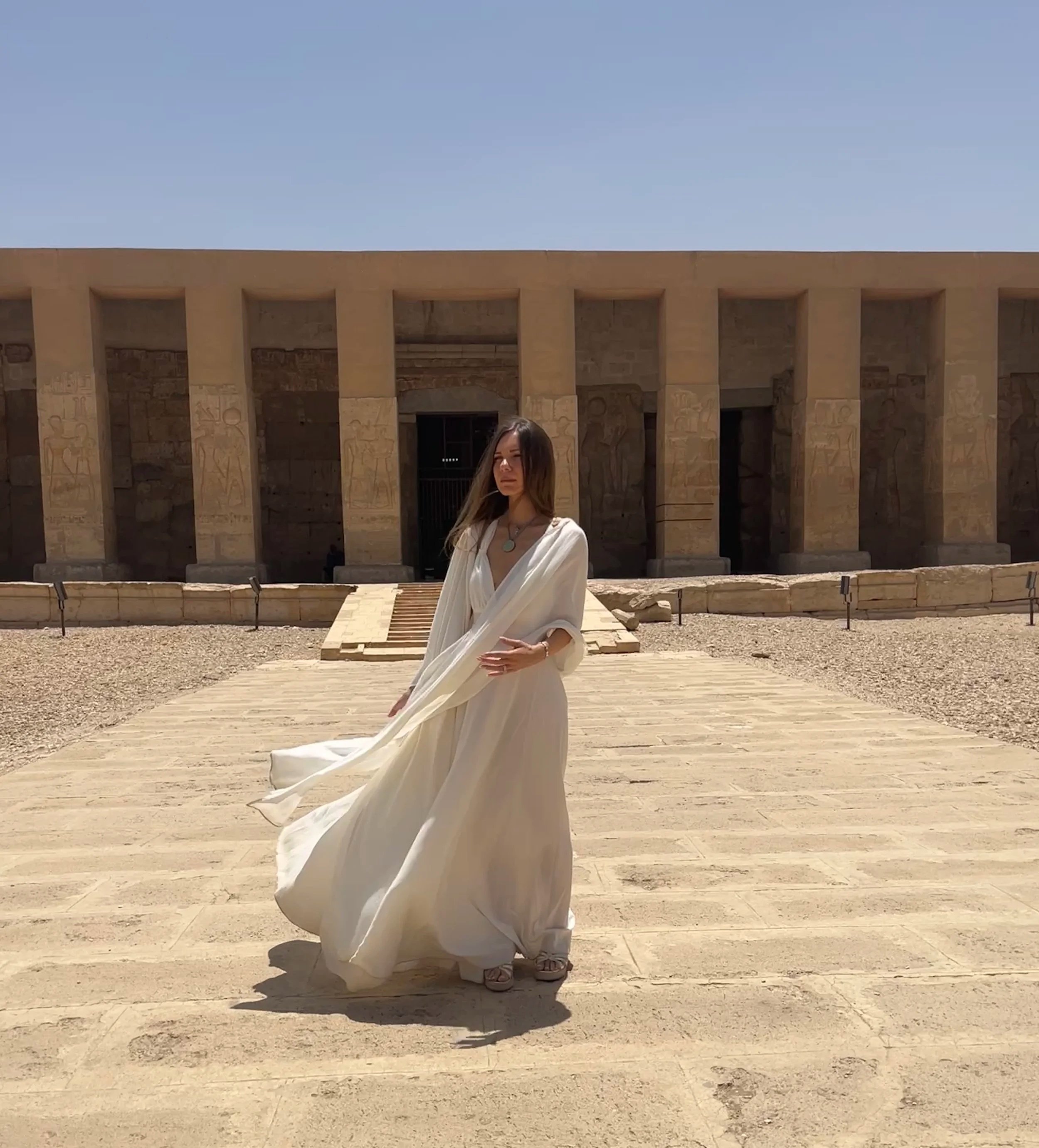 Sabina in flowing white dress standing in the courtyard of Abydos temple in Egypt
