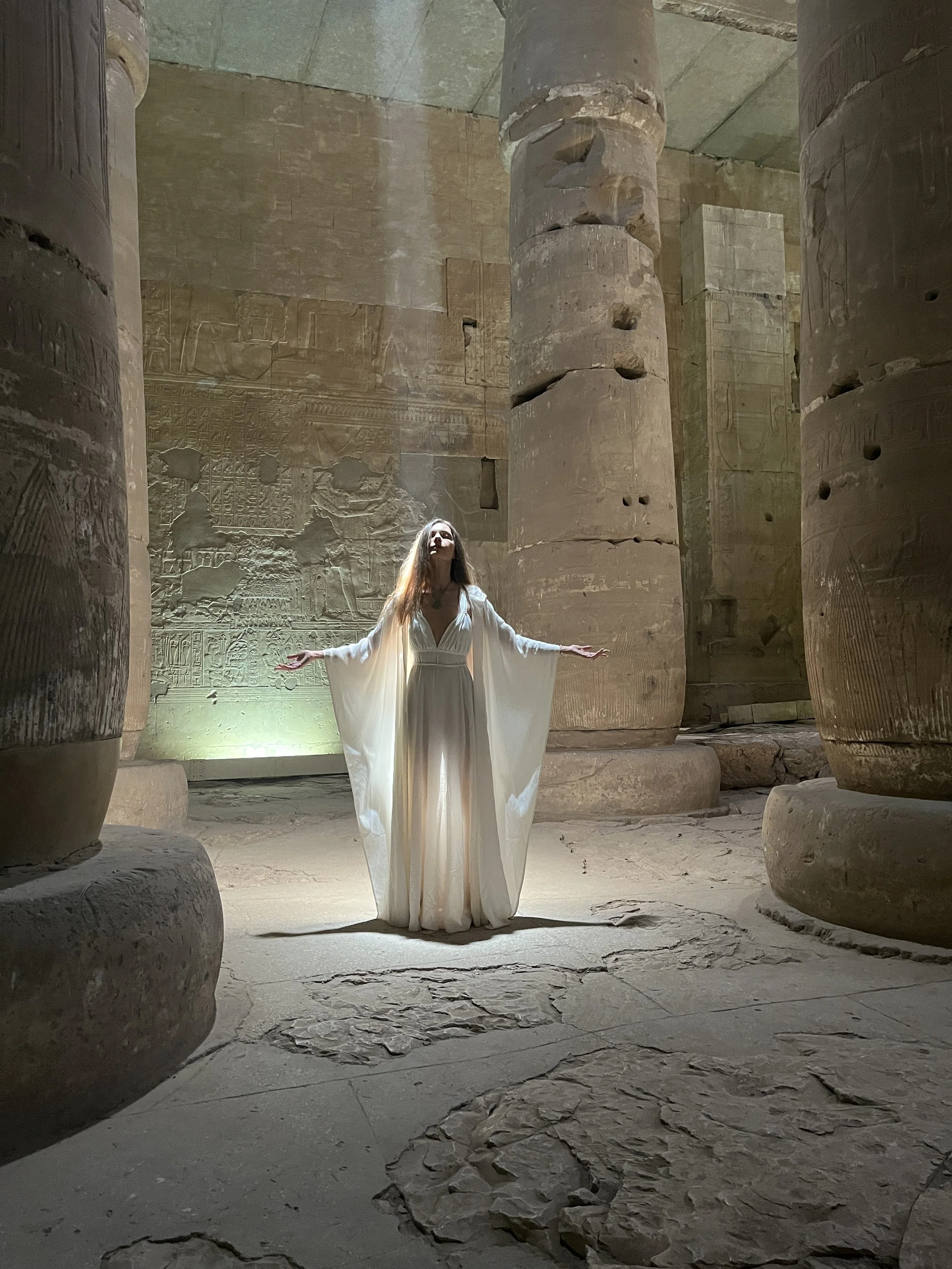 Sabina in white dress with arms open wide in sacred presence inside the Temple of Seti I at Abydos Egypt
