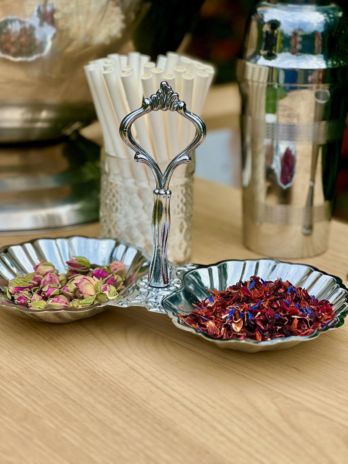 Plateau en métal avec des boutons de roses séchés et des pétales rouges, à côté d'un pot de pailles et d'un shaker argenté. Mobilier de bar à louer à Paris et Ile de France