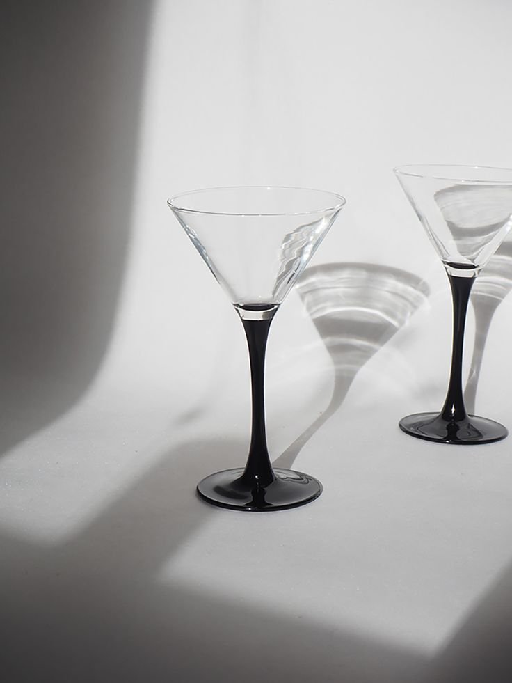 Deux verres à cocktail Martini transparents avec des pieds noirs sur une table blanche, à louer à Paris et Ile de France. Location de verres dépareillés.