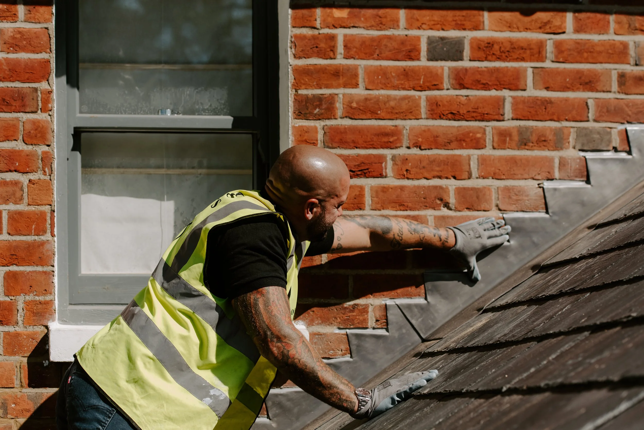 Roofer inspecting the flashing where a slate roof meets a brick wall