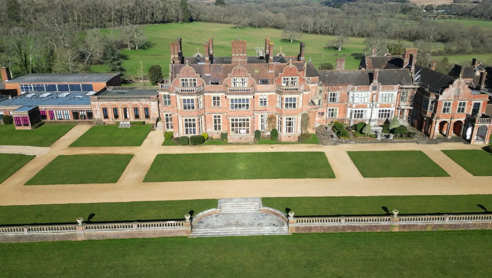 Heritage red-brick building with re-roofed pitched roofs and formal gardens, aerial view