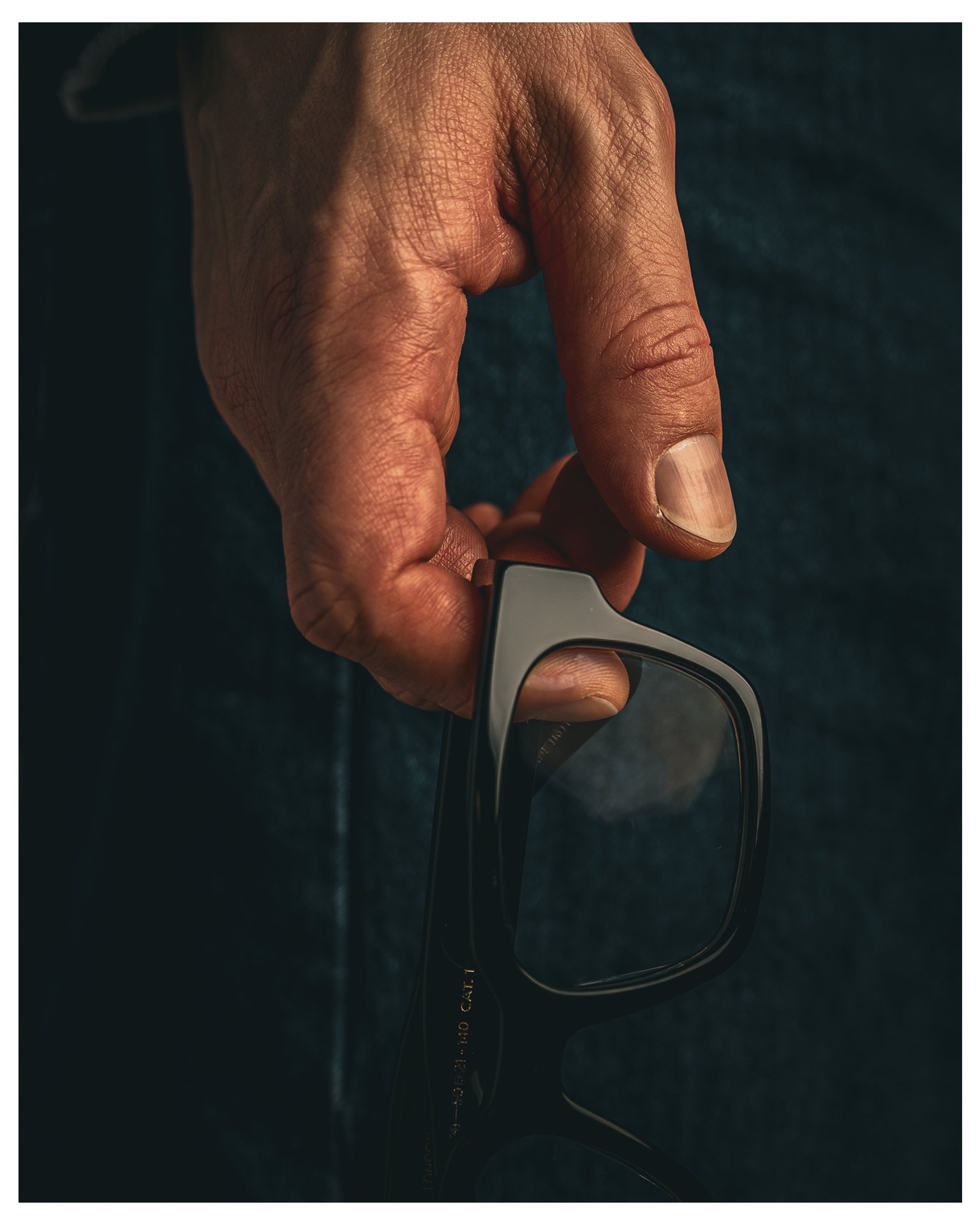 Nahaufnahme einer Hand, die eine schwarze Brille hält.