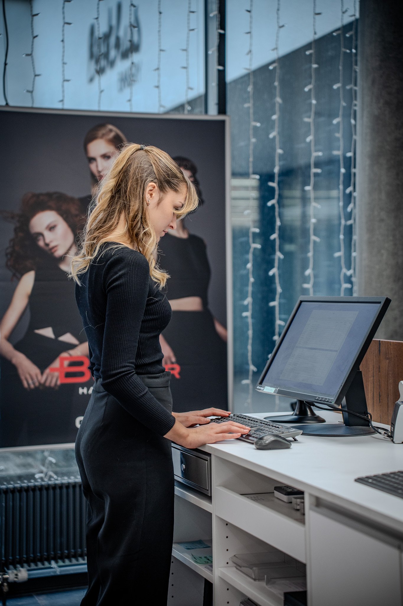 Frau arbeitet an einem Computer in einem modernen Büro mit Poster im Hintergrund.