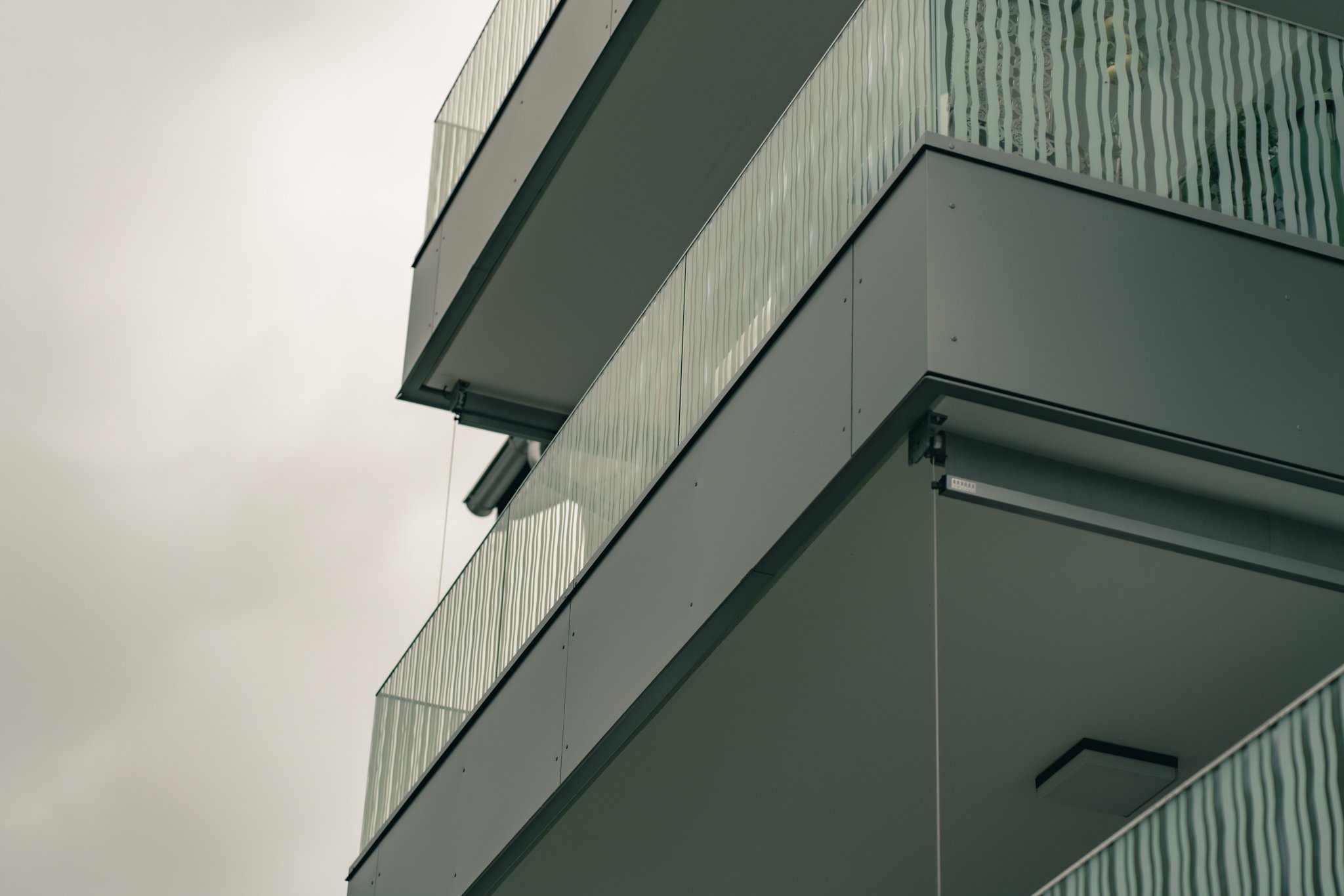 Moderne Balkone eines Gebäudes mit Glasgeländern und grauer Fassade.