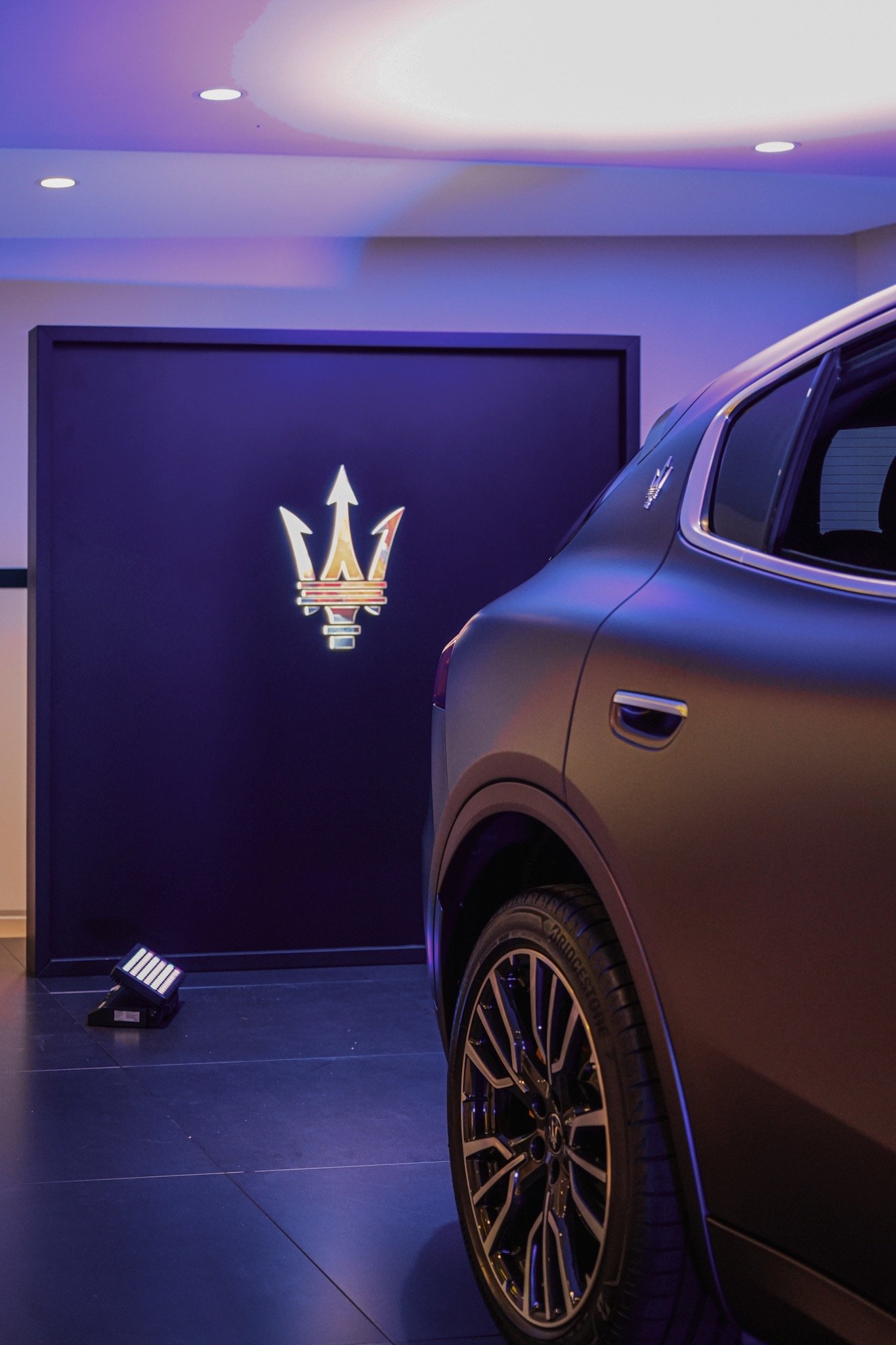 Maserati-Logo und Fahrzeug in einem stilvoll beleuchteten Raum.