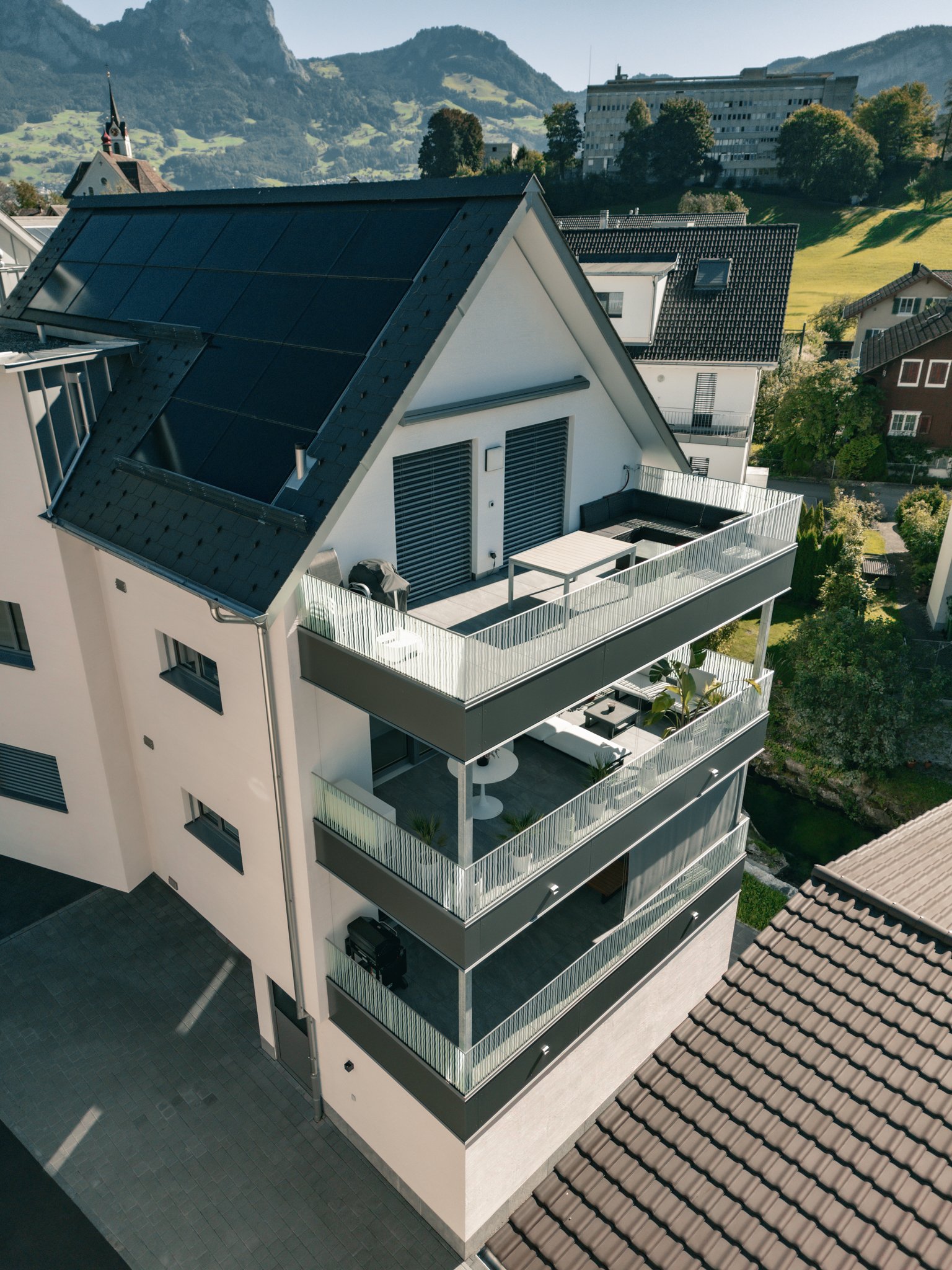Moderne mehrstöckige Wohnung mit Balkonen und Solardach in alpiner Landschaft.