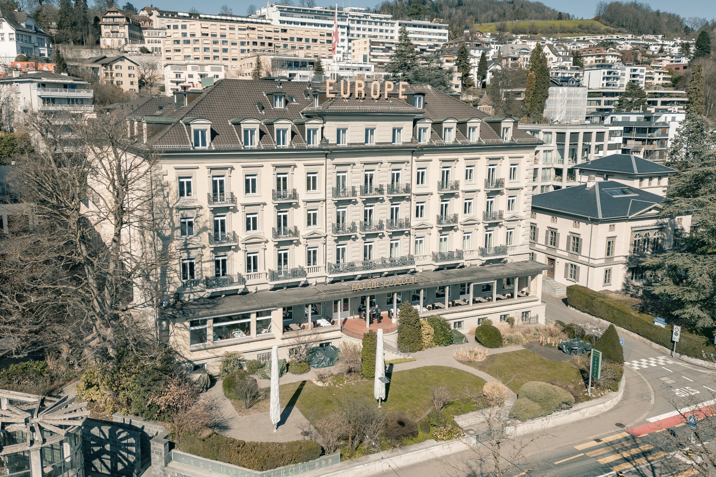 Historisches Gebäude mit dem Schriftzug "Europe" auf dem Dach, umgeben von modernen und traditionellen Gebäuden sowie Gärten im Vordergrund.