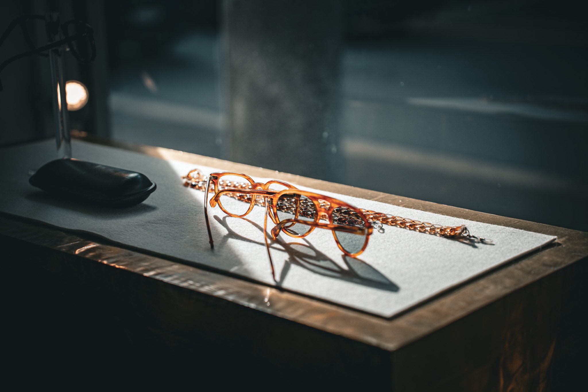 Braune Brille mit Kette auf einem Tisch mit Licht- und Schattenspiel.