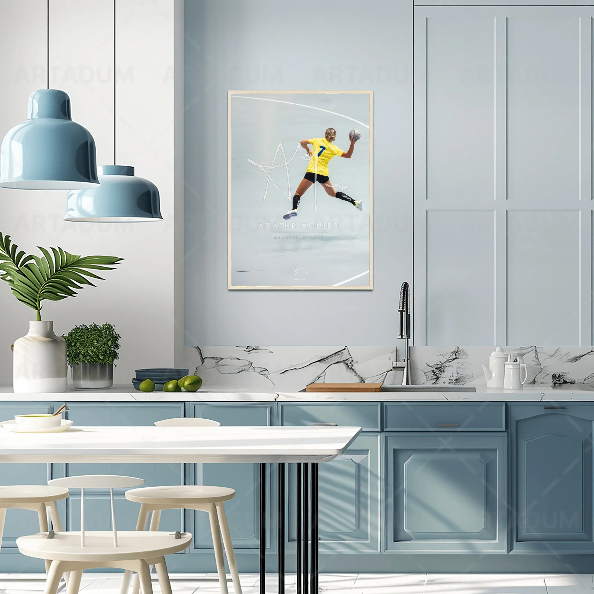 Cuisine moderne avec un mur gris clair, un plan de travail en marbre blanc et une peinture sportive d'une joueuse de sport en jaune. Il y a des plantes vertes en pot sur le comptoir, une table blanche avec des chaises. Un robinet noir à côté de l'évier.