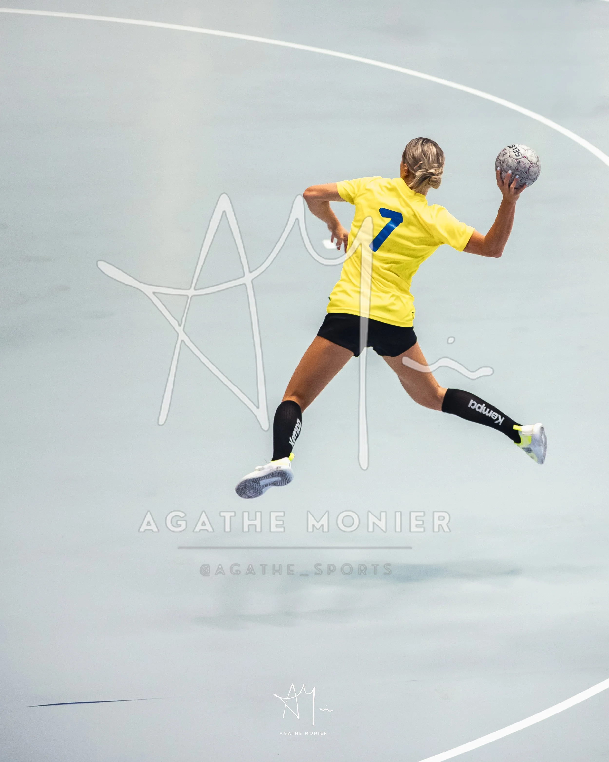 Une joueuse de handball en plein saut, portant un maillot jaune avec le numéro 7, tenant un ballon de handball.