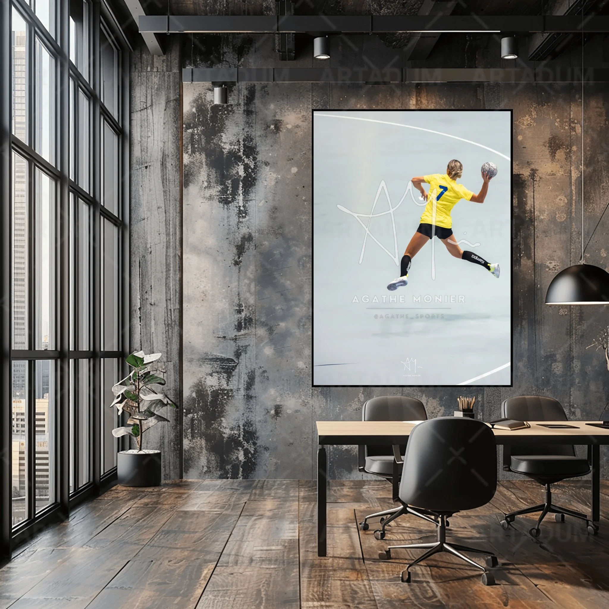 Une salle de conférence moderne avec un mur en béton, une grande affiche d'une joueuse de handball en saut, portant un maillot jaune, avec un ballon. Il y a une table de réunion en bois, des chaises noires, un lampadaire noir suspendu et une plante dans un pot noir près de la fenêtre.