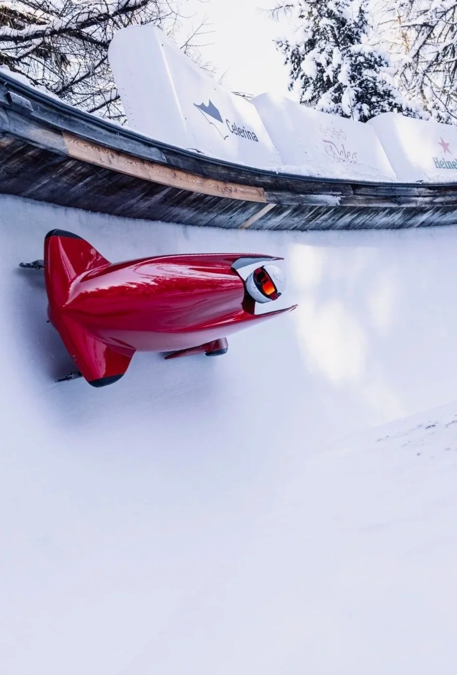 Red futuristic snowmobile on snowy ground, with an overturned boat with decals and graffiti in the background, in a winter outdoor setting.