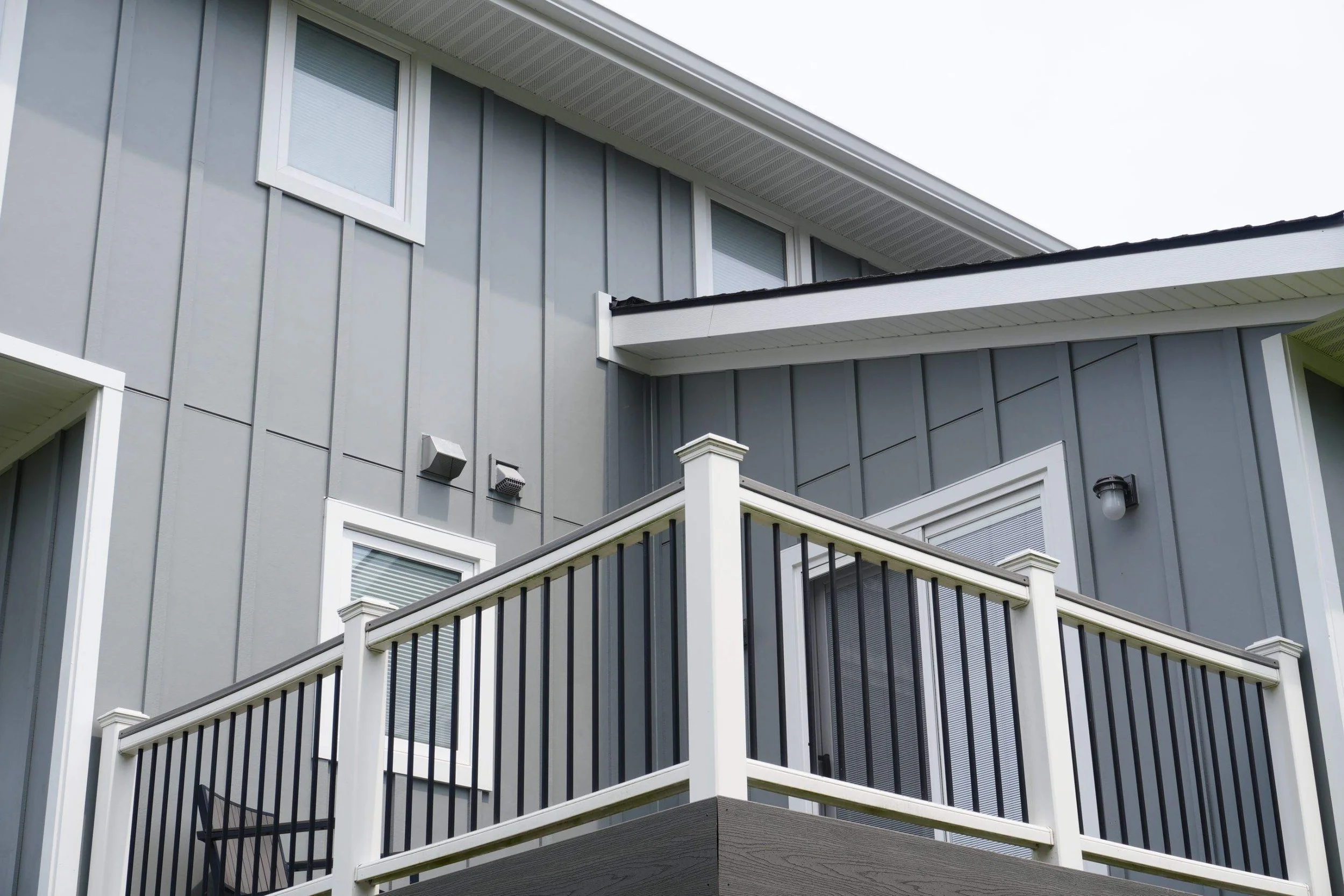 Close-up of this modern Michigan home’s gray exterior, featuring a balcony, windows, and lighting fixtures. The renovation includes James Hardie Board and Batten in Gray Slate, Arctic White trim, Quality Edge soffit and fascia, and 6” seamless gutter