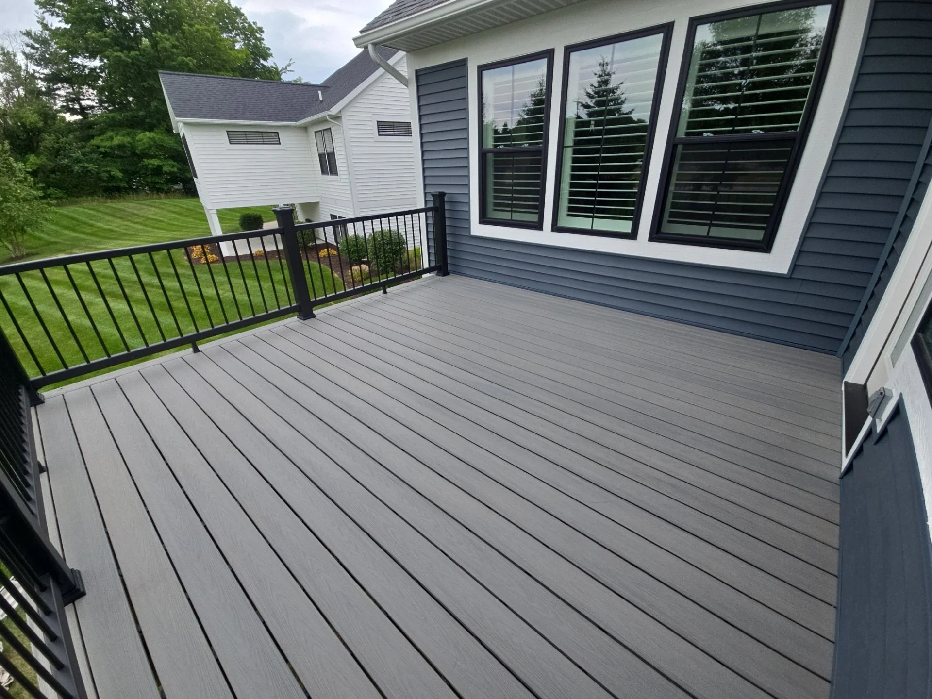 We built this deck from the ground up with gray Decorators decking, black Trex composite railings, and LP wood grain trim, perfectly complementing the home’s blue siding and large windows.