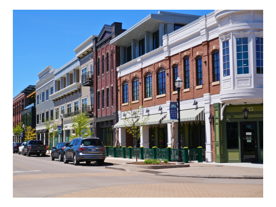 Street view of a row of modern commercial and residential buildings with cars parked along the curb on a sunny day.