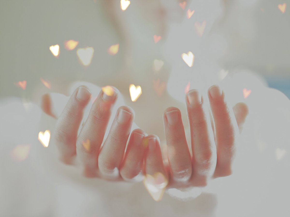 Hands reaching upward with a soft overlay of glowing heart shapes.