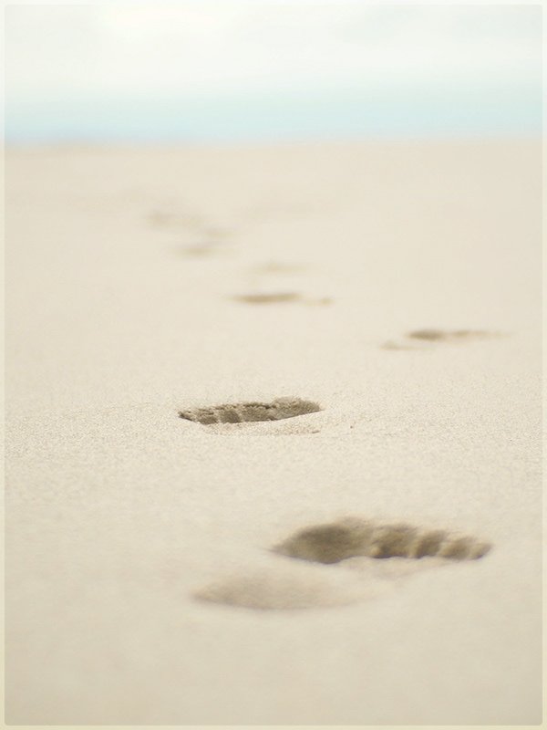 Footprints in the sand leading into the distance on a beach.