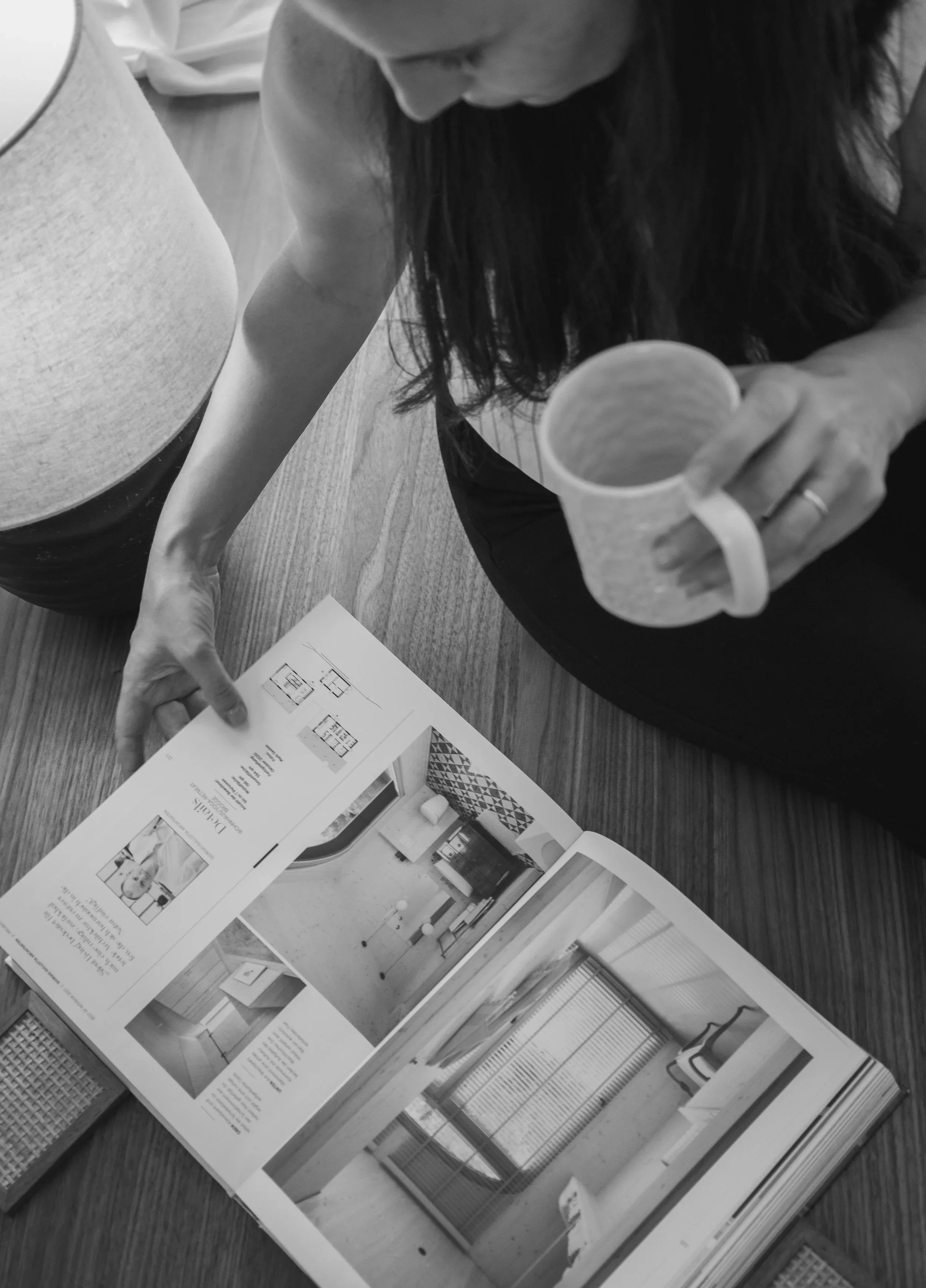 Persona revisando un folleto con imágenes de interiores y planos en una mesa de madera.