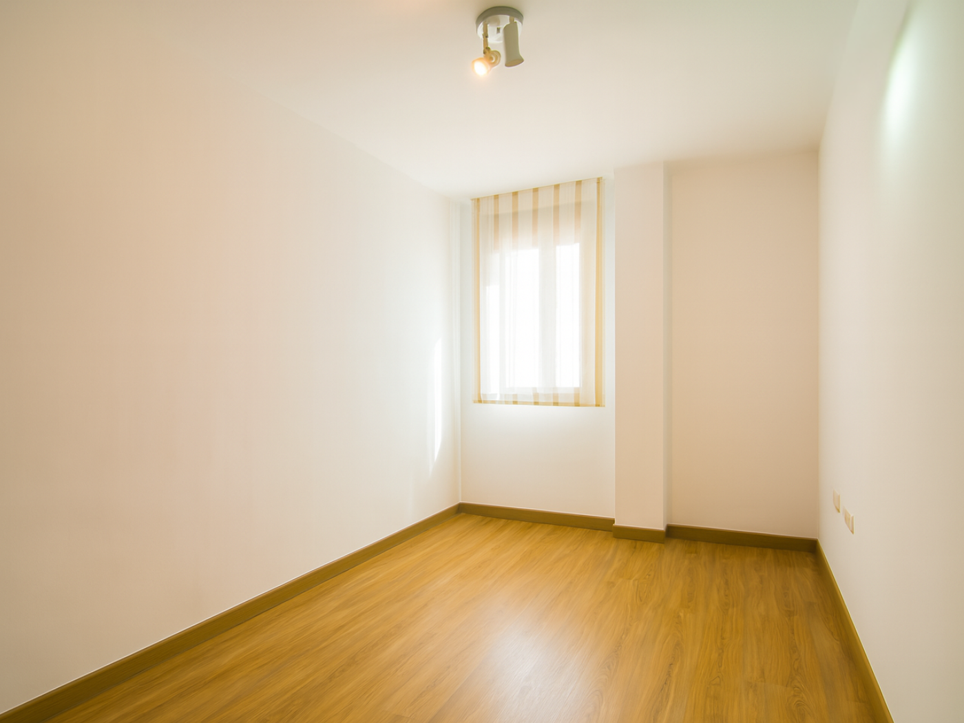 Dormitorio angosto y alargado vacio con ventana con cortina tipo store.