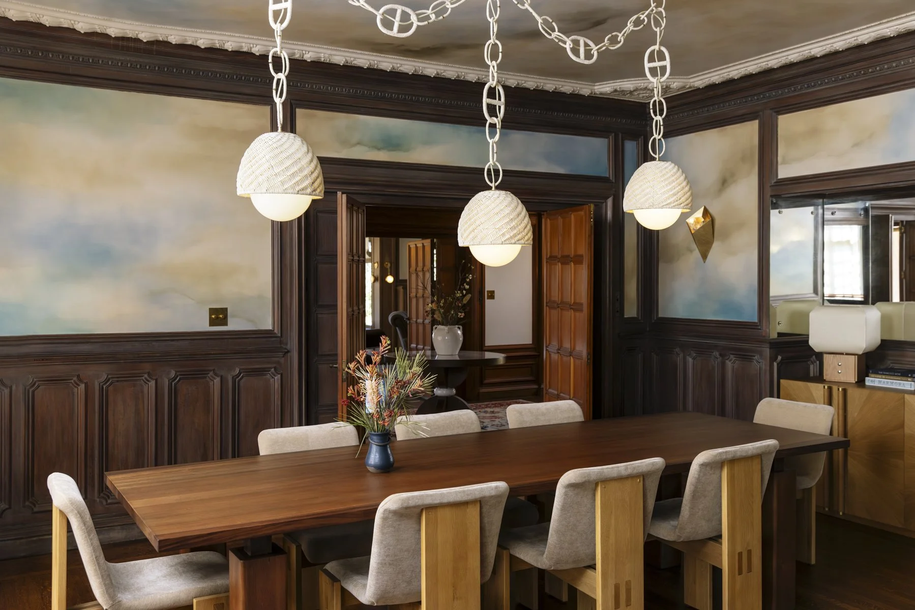 Luxury dining room renovation in a San Francisco home featuring custom wood paneling, a handcrafted solid wood dining table, upholstered oak dining chairs, designer pendant lighting with decorative chain suspension, painted ceiling mural, and restore