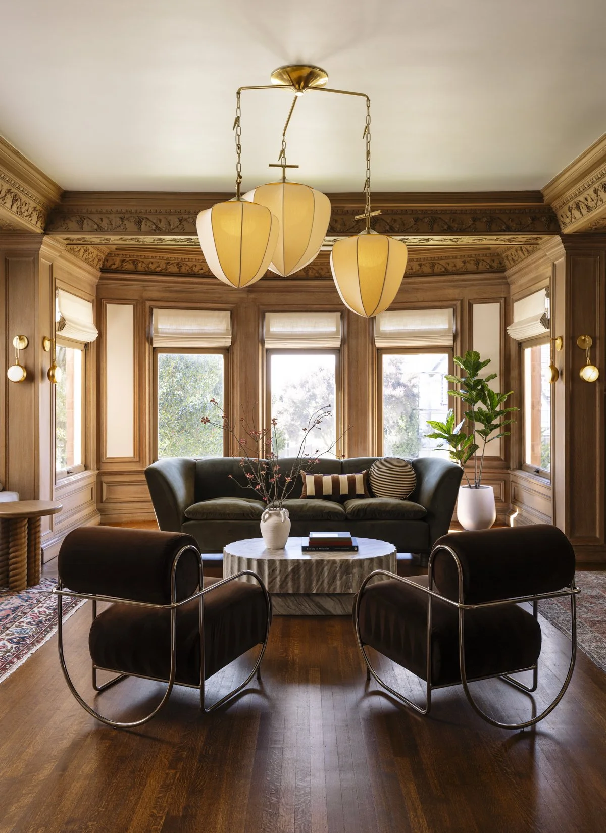 Luxury living room renovation in a historic San Francisco home featuring original wood paneling, large bay windows, custom lighting, hardwood floors, modern furniture, and abundant natural light that highlights the restored architectural details.