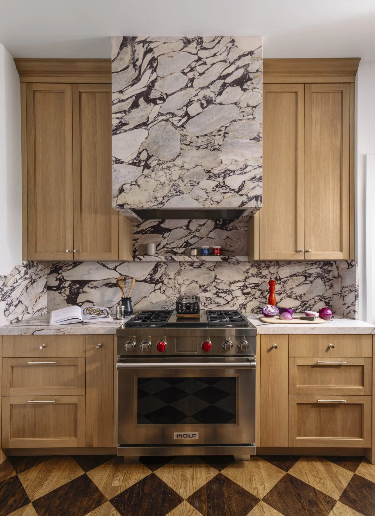 Luxury kitchen renovation featuring a Wolf range with a full-height marble range hood and backsplash, white oak shaker cabinets, custom millwork, and a patterned hardwood floor in a historic San Francisco home.