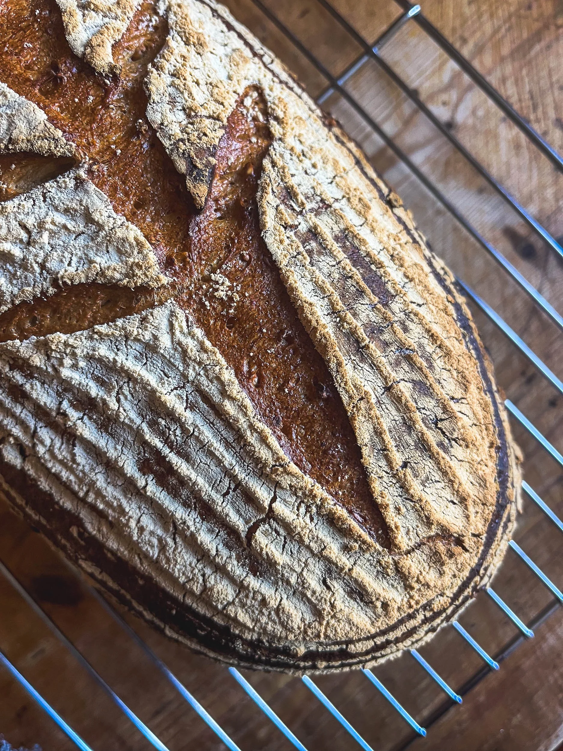 Close-up of a freshly baked loaf of bread with a rustic crust, cooling on a wire rack over a wooden surface.