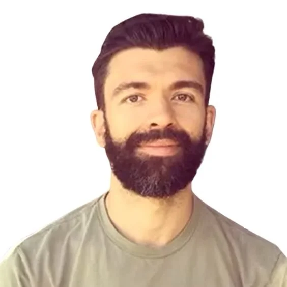 A man with dark hair and a full beard, smiling slightly, wearing a gray T-shirt, against a plain white background.