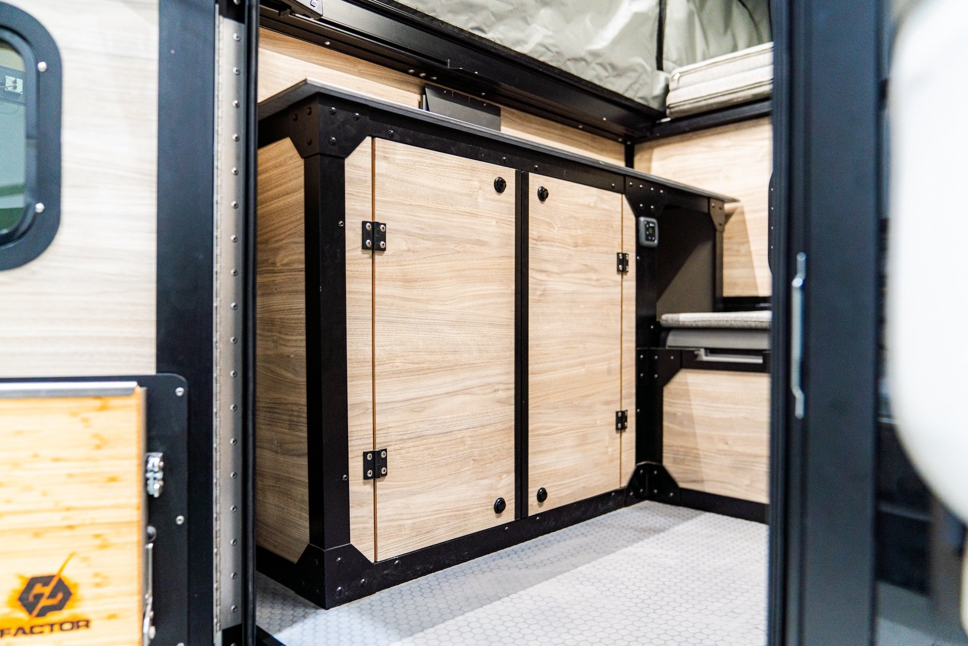 Interior of a camper with light wood cabinets, black metal framing, and a patterned floor.