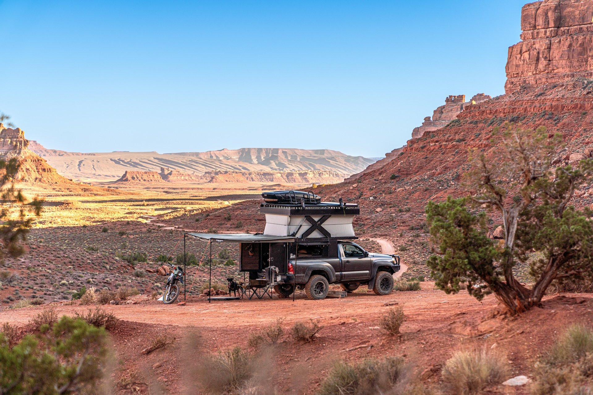 Overlanding vehicle with a roof tent and awning in a desert landscape with red rock formations.