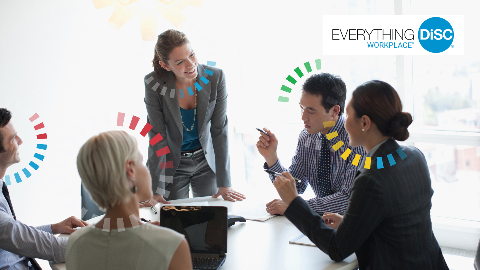 Business team in a meeting with a woman standing and engaging with colleagues seated around a table, in a bright office with large windows, with overlaying colorful loading circle graphics and 'EVERYTHING DISC WORKPLACE' logo.