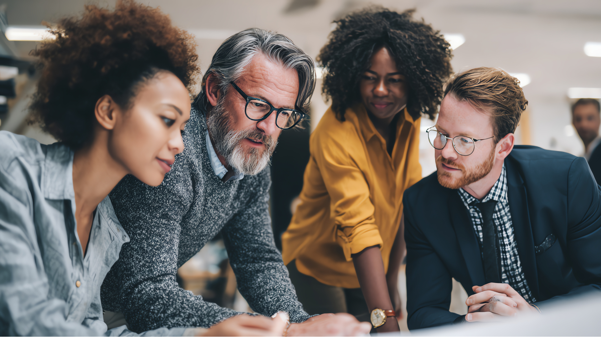 Four diverse professionals collaborating in an office workshop, looking at multiple resources together.