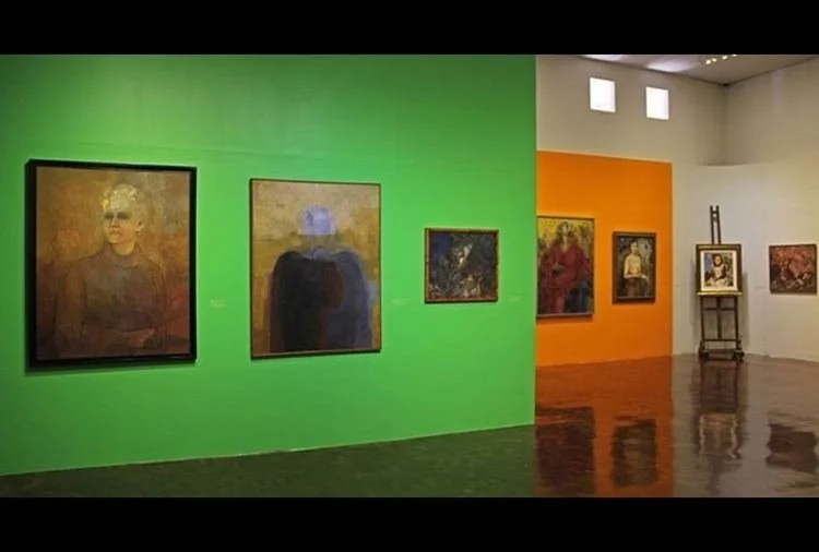 Art gallery with colorful walls featuring various paintings, including portraits and abstract art.