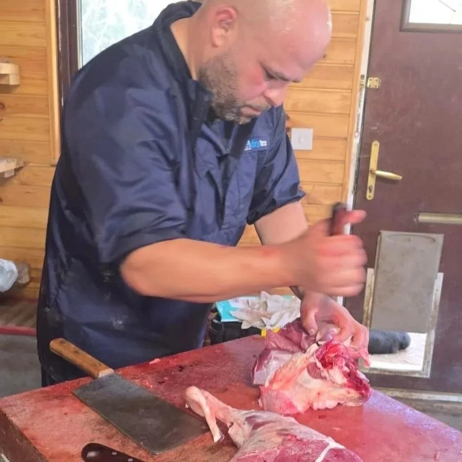 Mobile Slaughterman Richard cutting meat on a butcher's block using a knife and cleaver