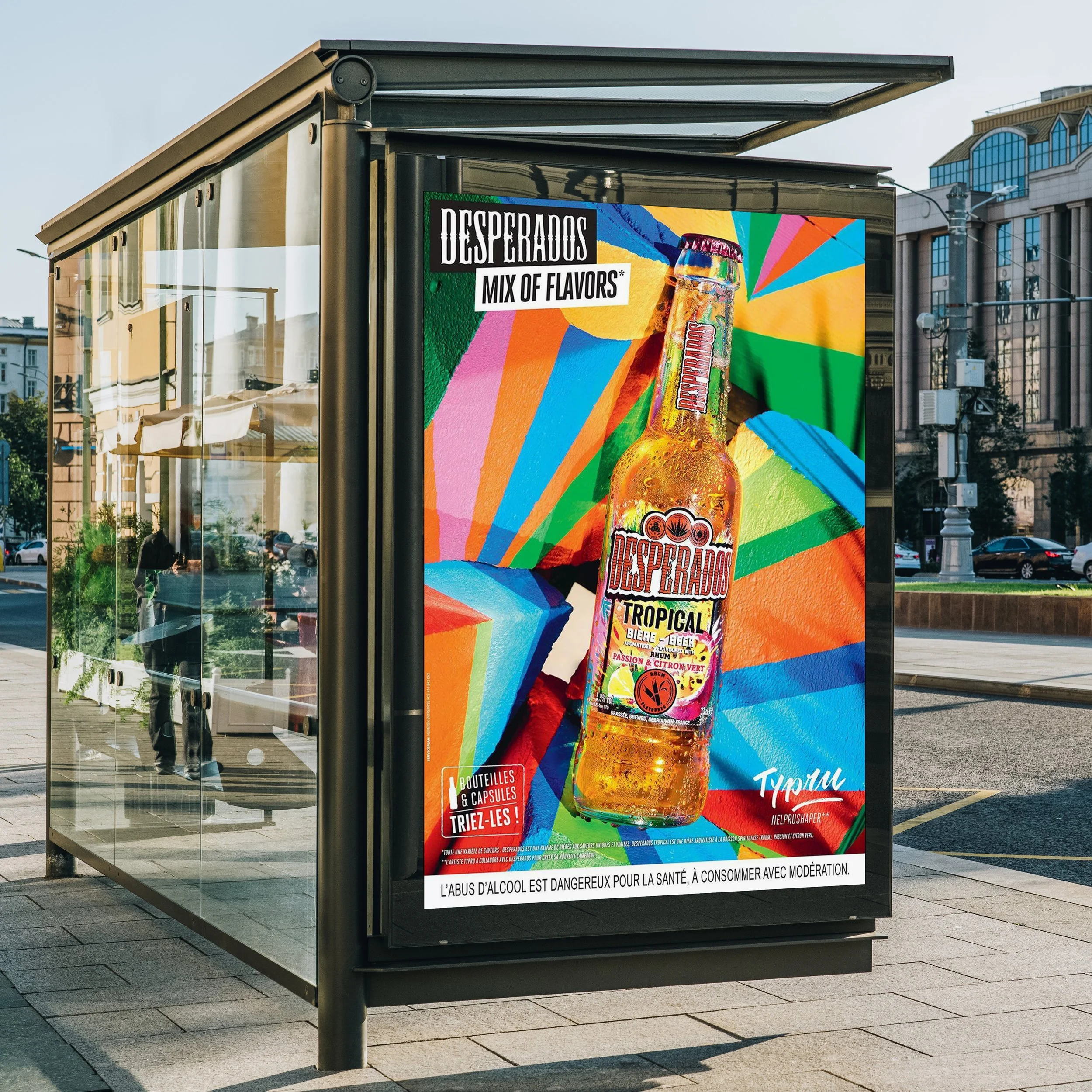Advertisement display for Desperados Tropical beer featuring a colorful abstract background with a large beer bottle in the center. The text highlights a mix of flavors and promotes the product.