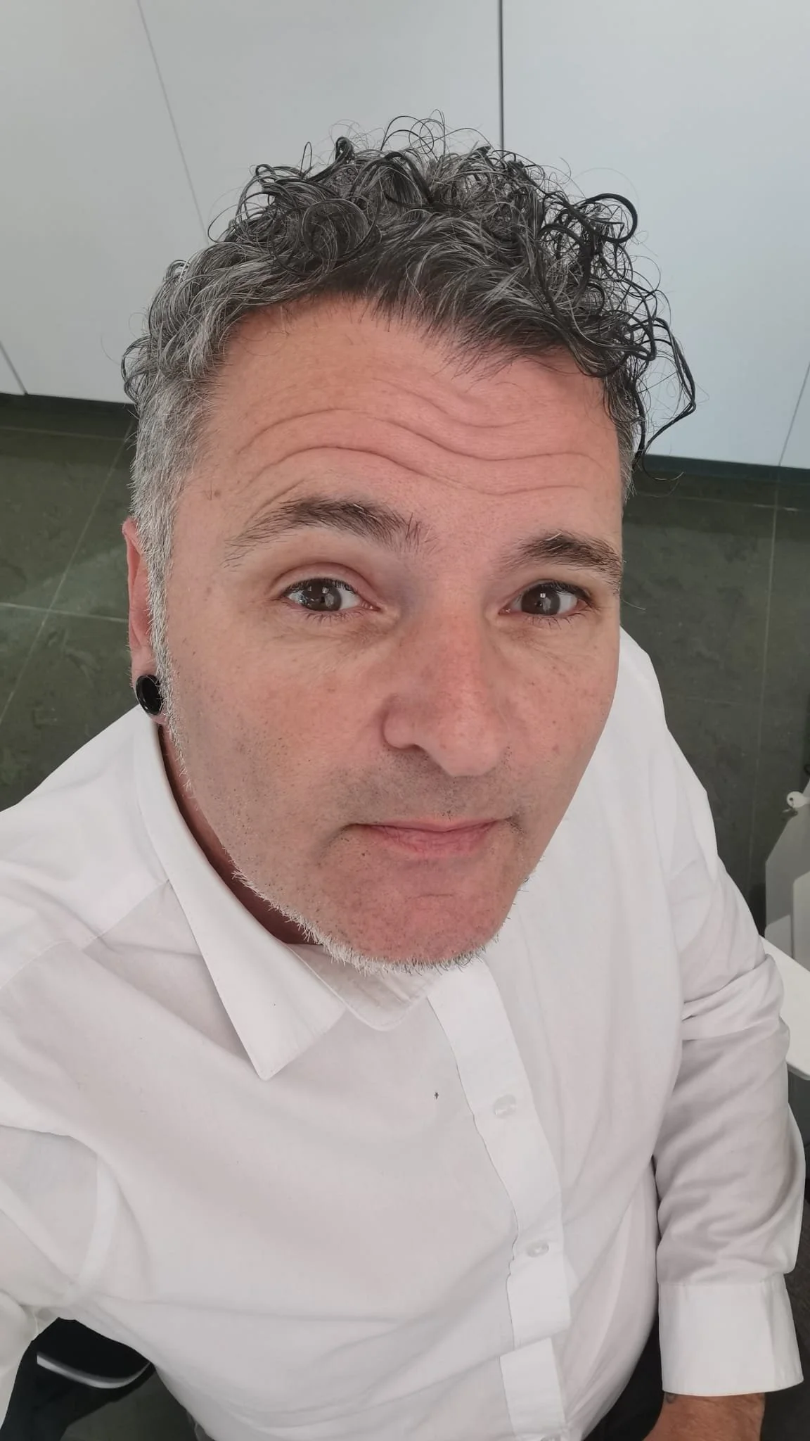 Man with gray curly hair wearing a white shirt looking at camera.