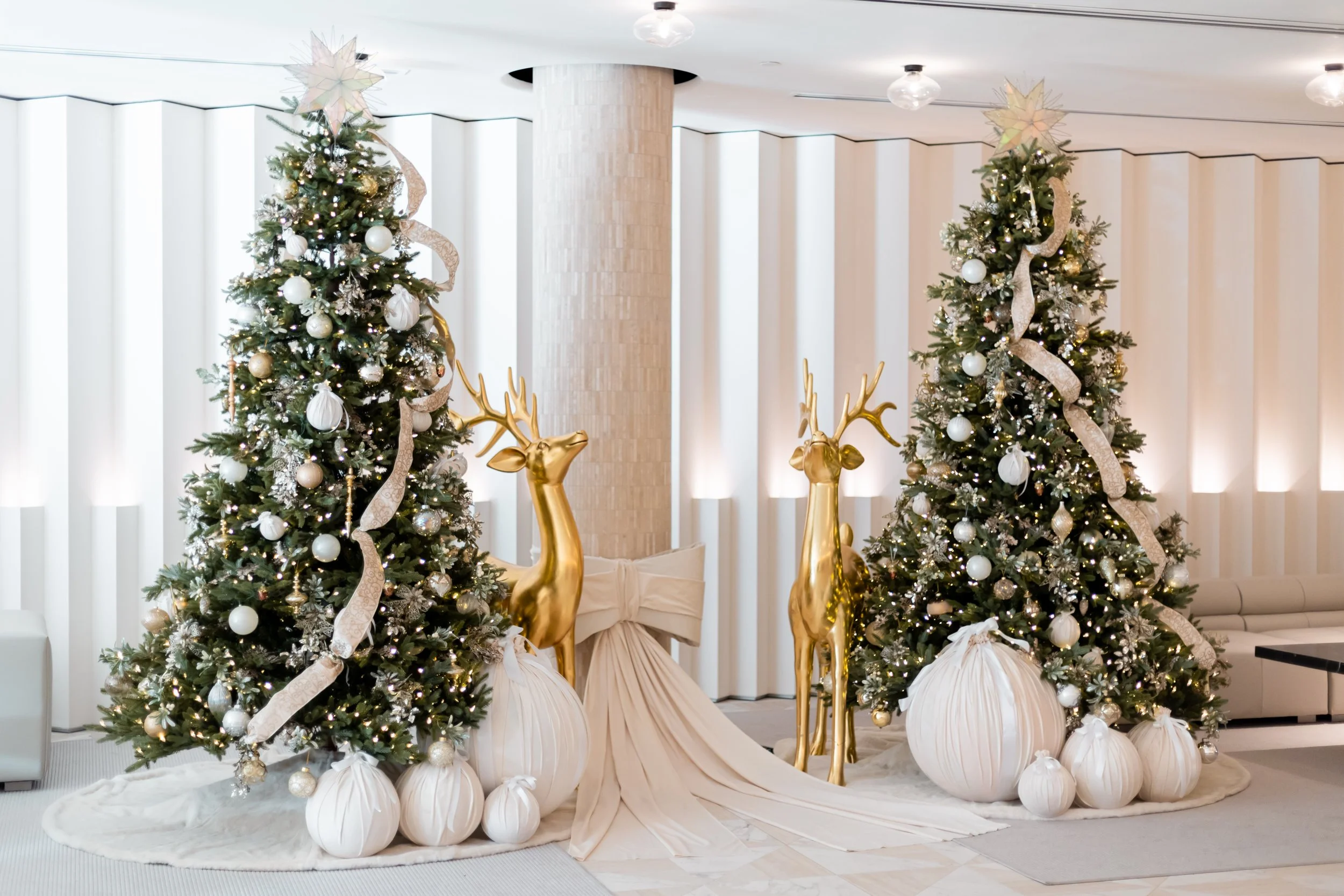 A majestic holiday display of symmetrical, softly-illuminated festive trees adorned with designer gold and pearl ornaments, flawlessly styled alongside majestic gilded reindeer sculptures.