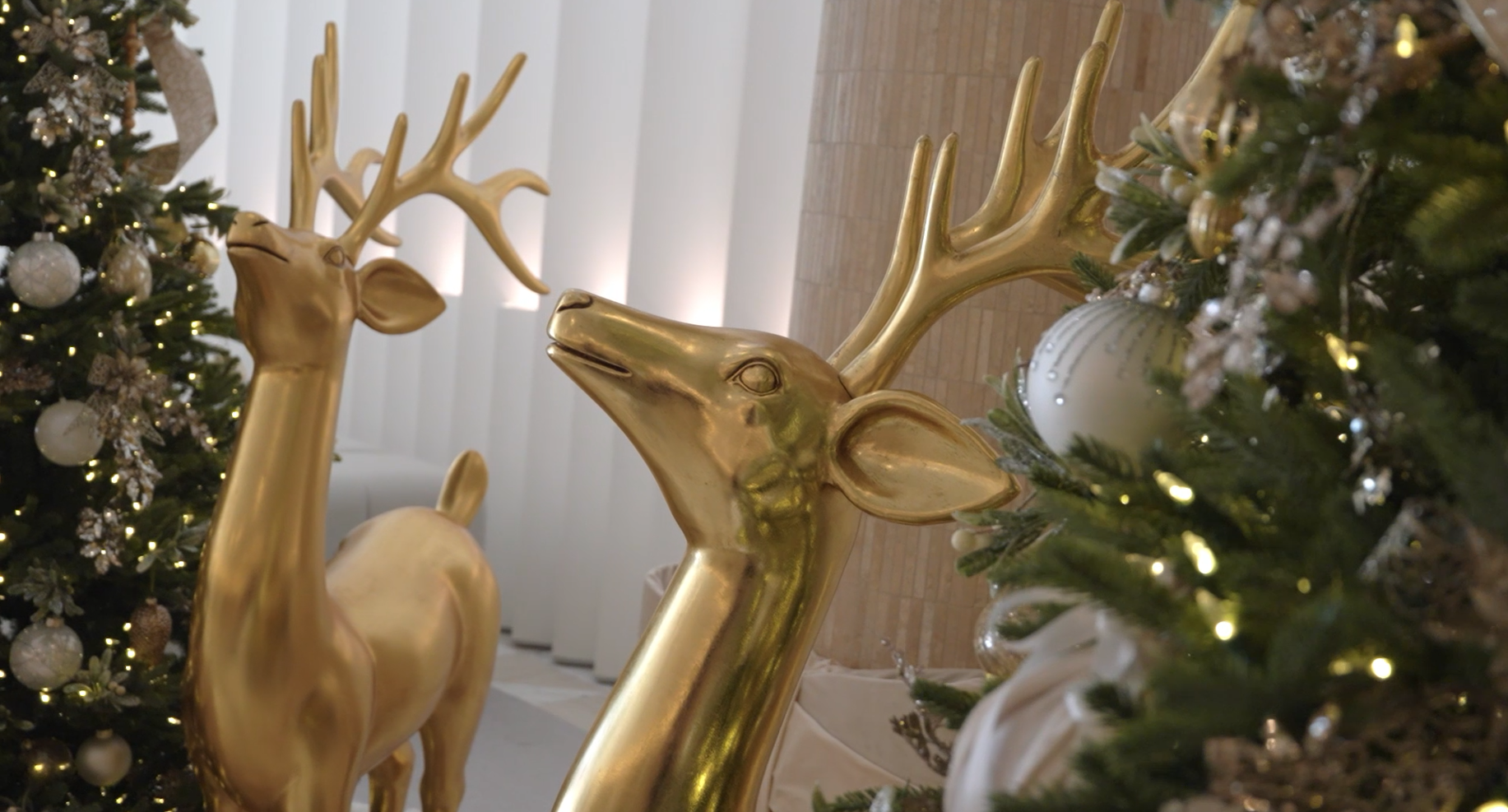 A detailed shot of a majestic, antique-style gold reindeer sculpture positioned beautifully within a backdrop of illuminated holiday foliage and frosted white berries.