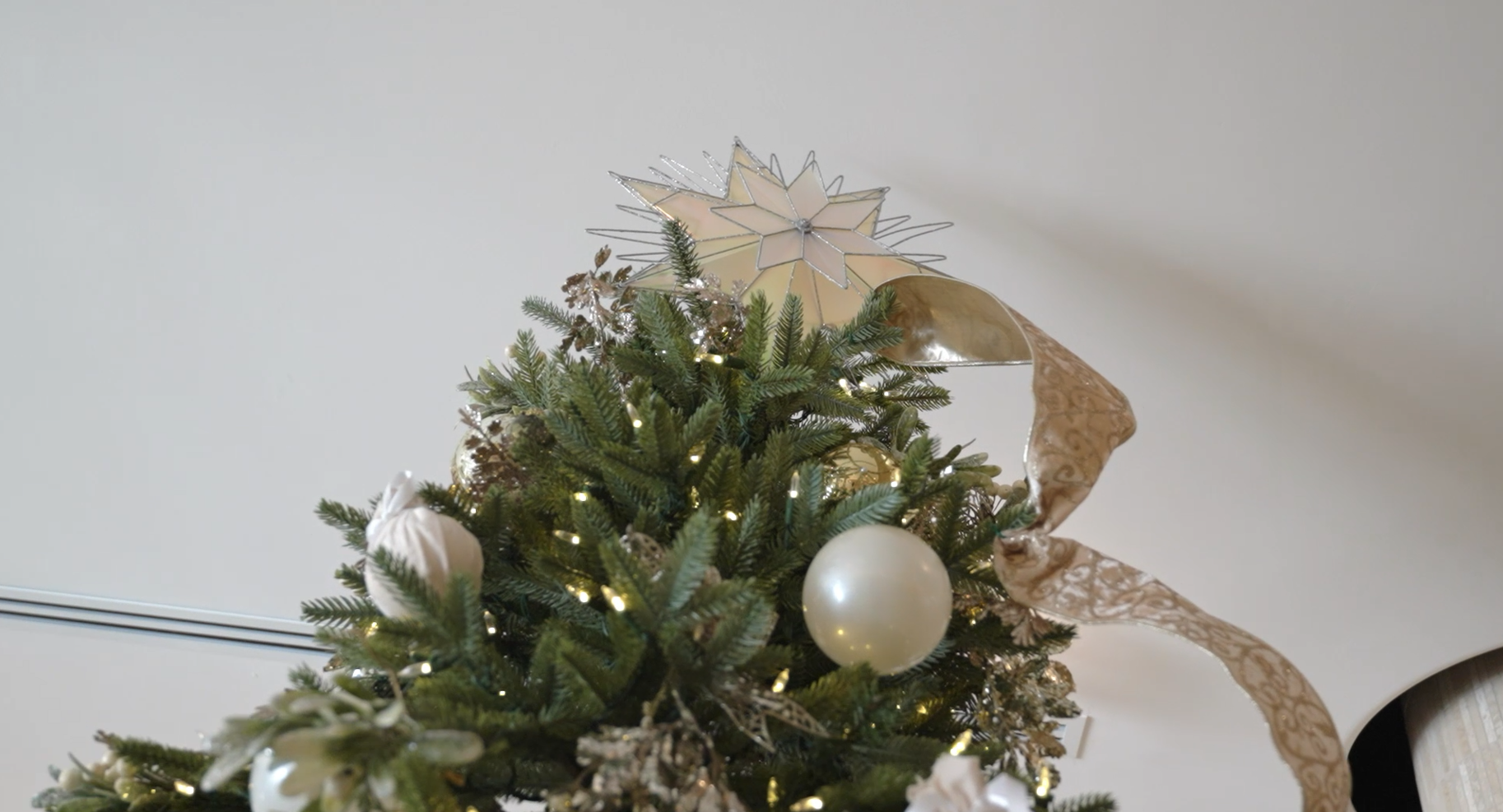 An exquisite close-up of a matte white ceramic bauble, meticulously detailed with a delicate, raised gold starburst lattice pattern hanging from a frosted pine branch.