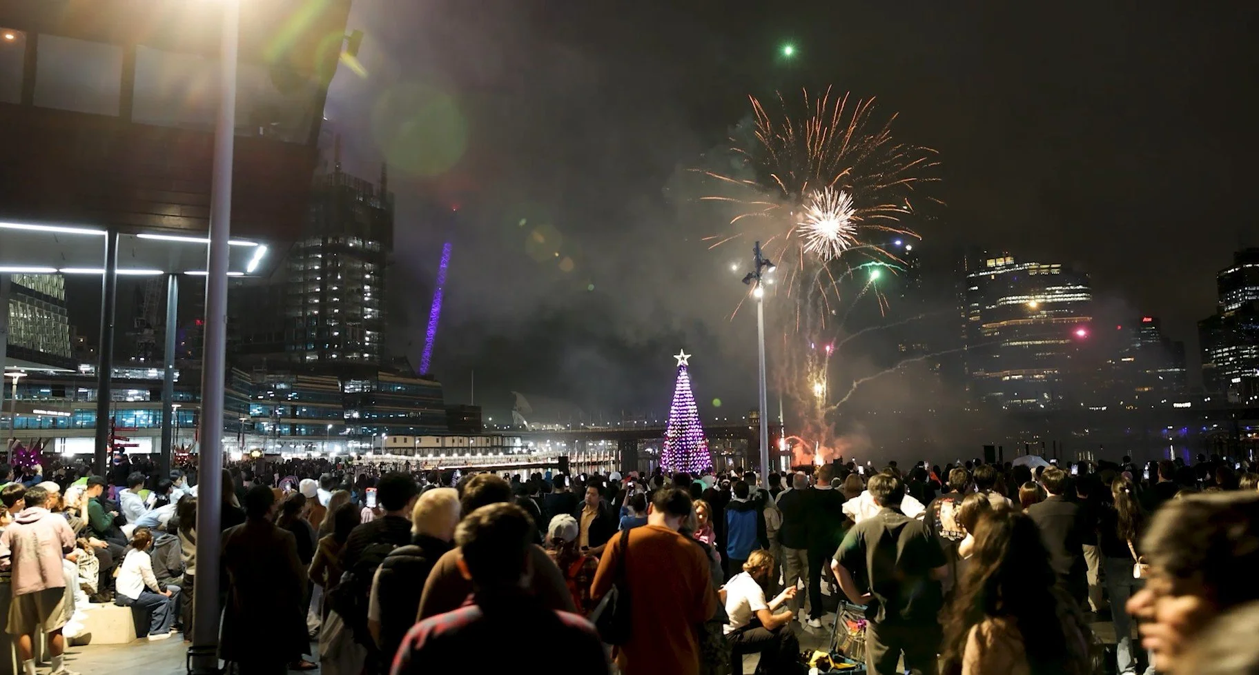 A stunning night view of the Cockle Bay Christmas tree lighting ceremony with fireworks bursting in the background.