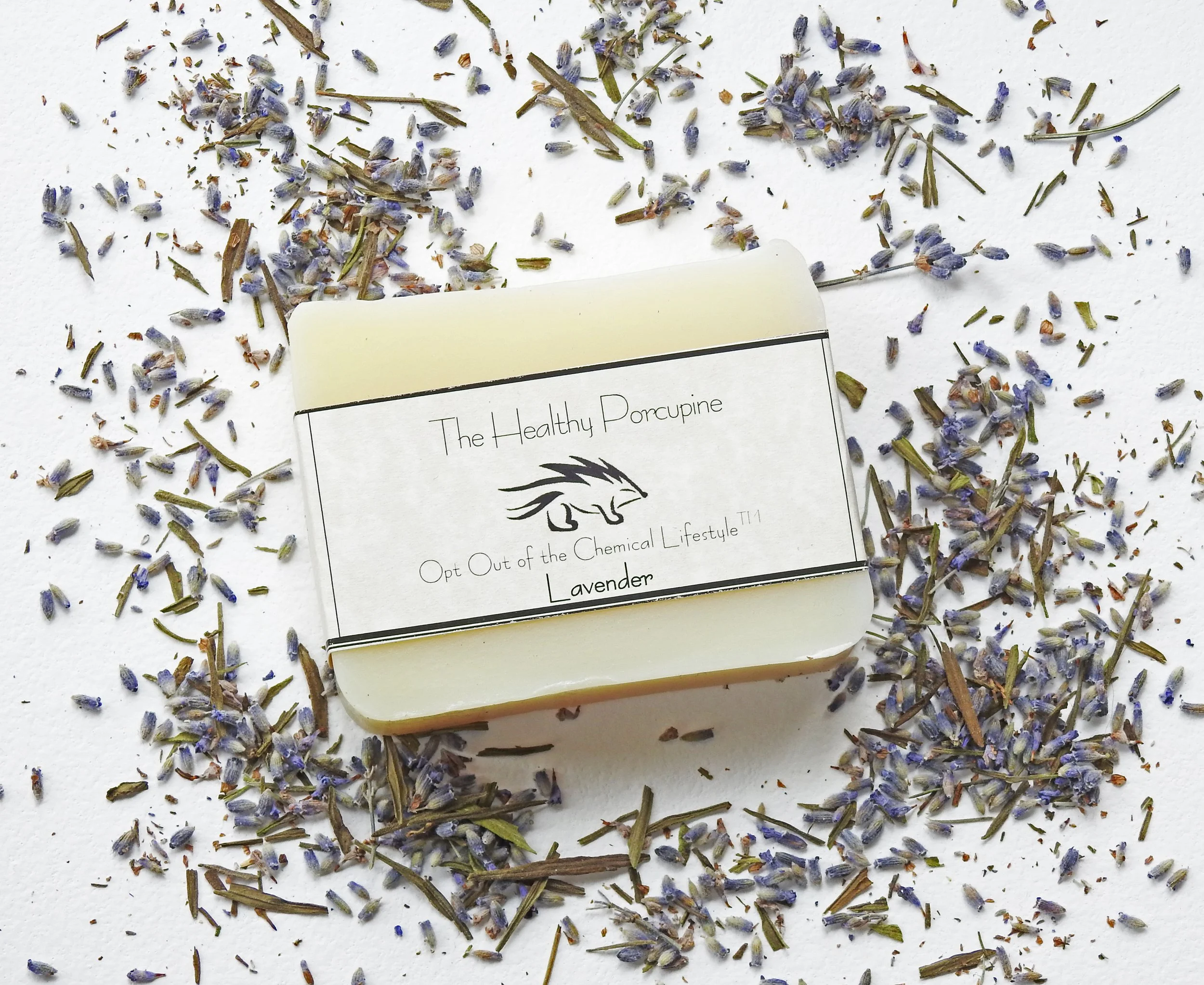 A bar of lavender soap labeled 'The Healthy Porcupine' surrounded by dried lavender flowers and leaves on a white surface.