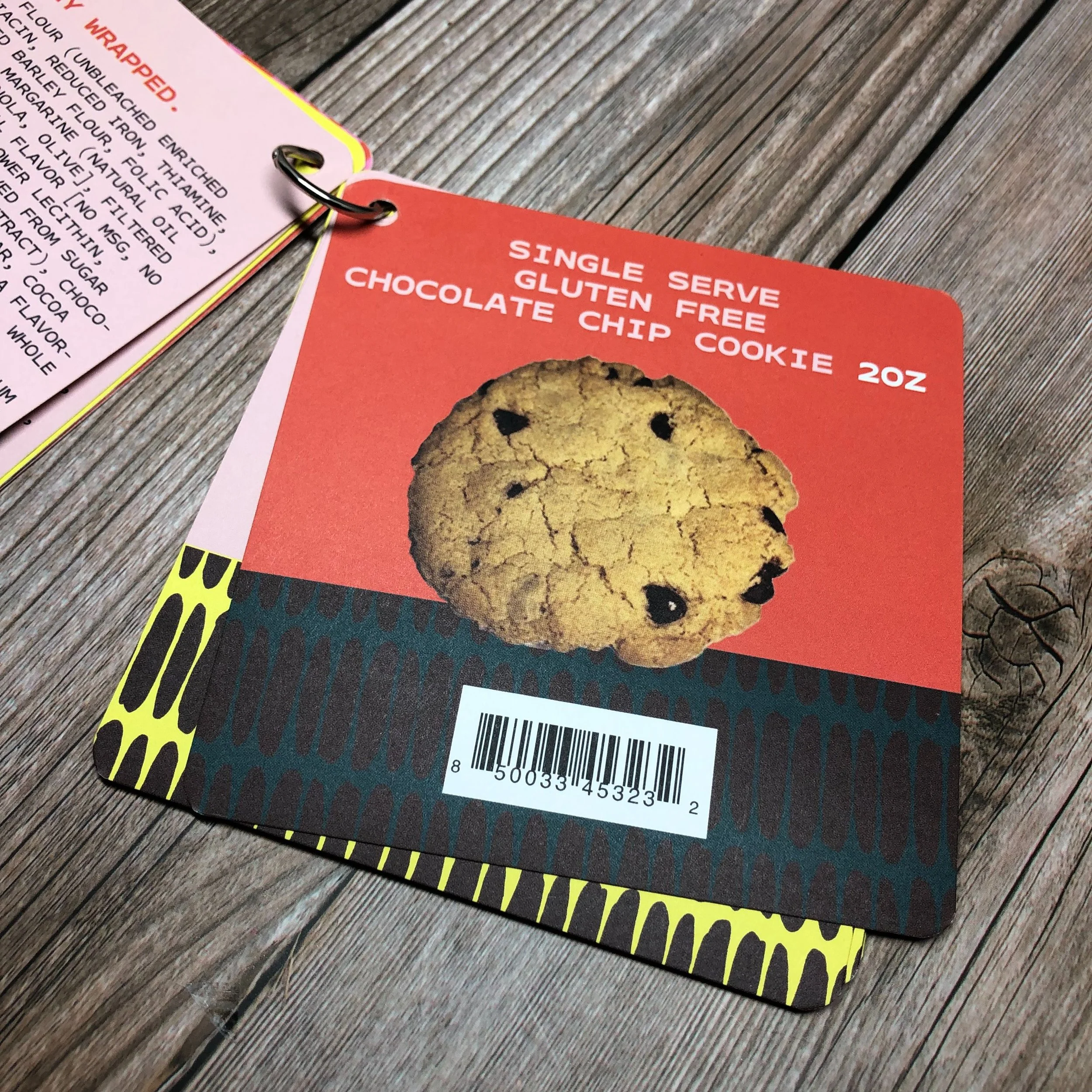 Advertisement for a single serve, gluten-free chocolate chip cookie, 2 ounces, featuring a picture of a chocolate chip cookie on a colorful card.