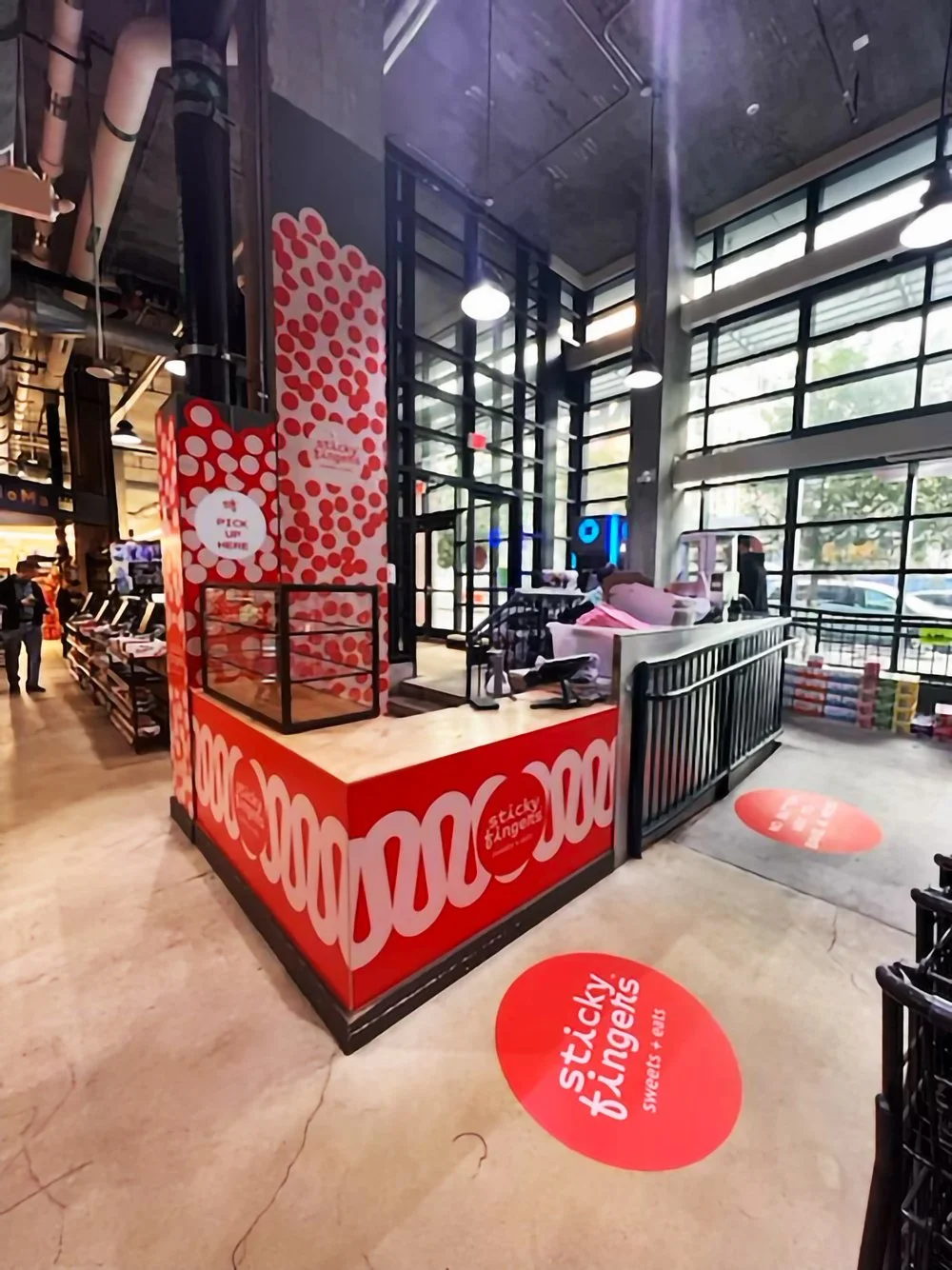 Interior of a Sticky Fingers store with a red and white branded counter and sign, large glass windows, and a few customers shopping